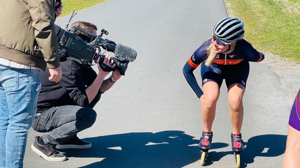Vrouw op skeelers benadert een cameraman op een weg.
