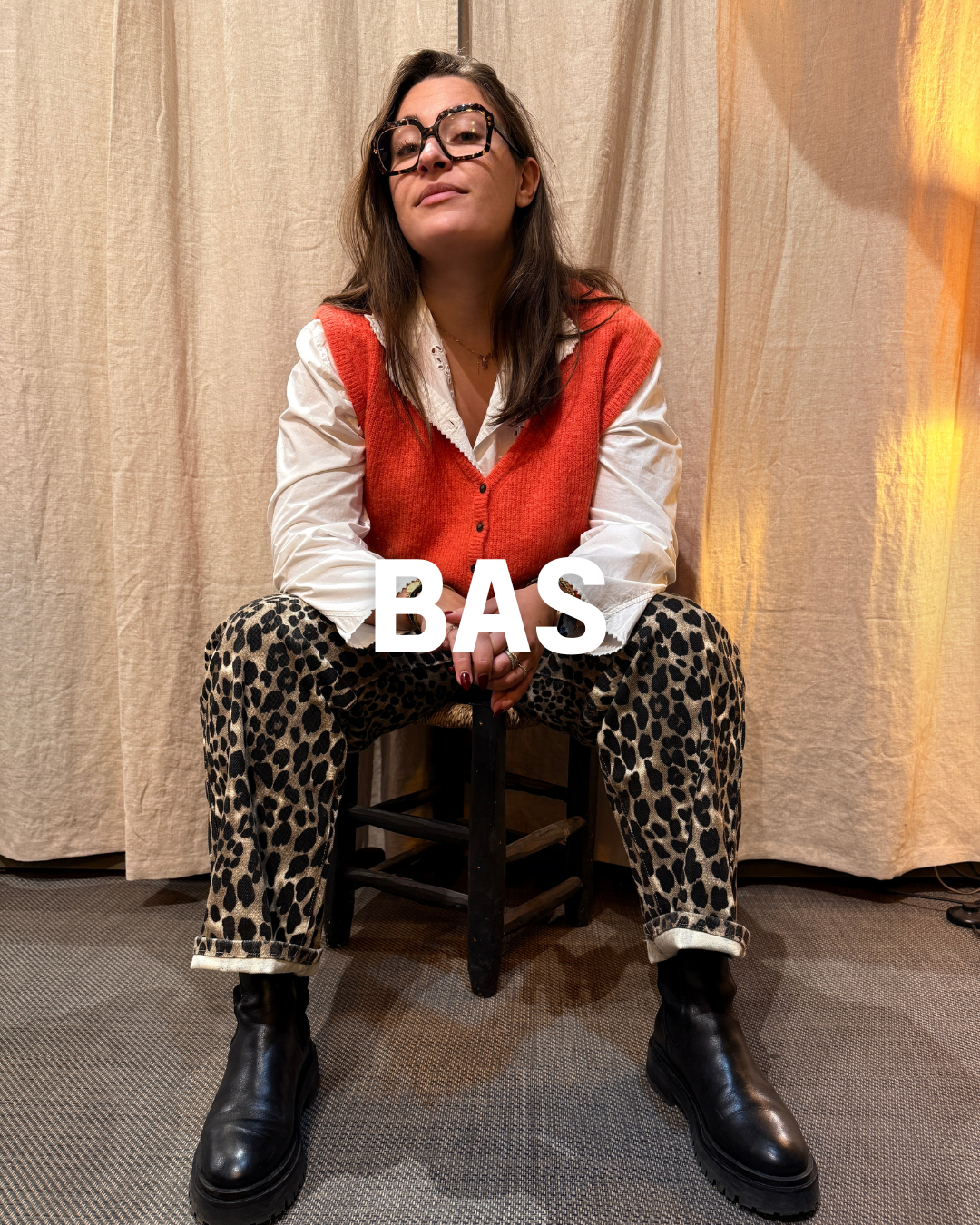 Femme assise sur un tabouret avec un pantalon leopard et un gilet orange 
