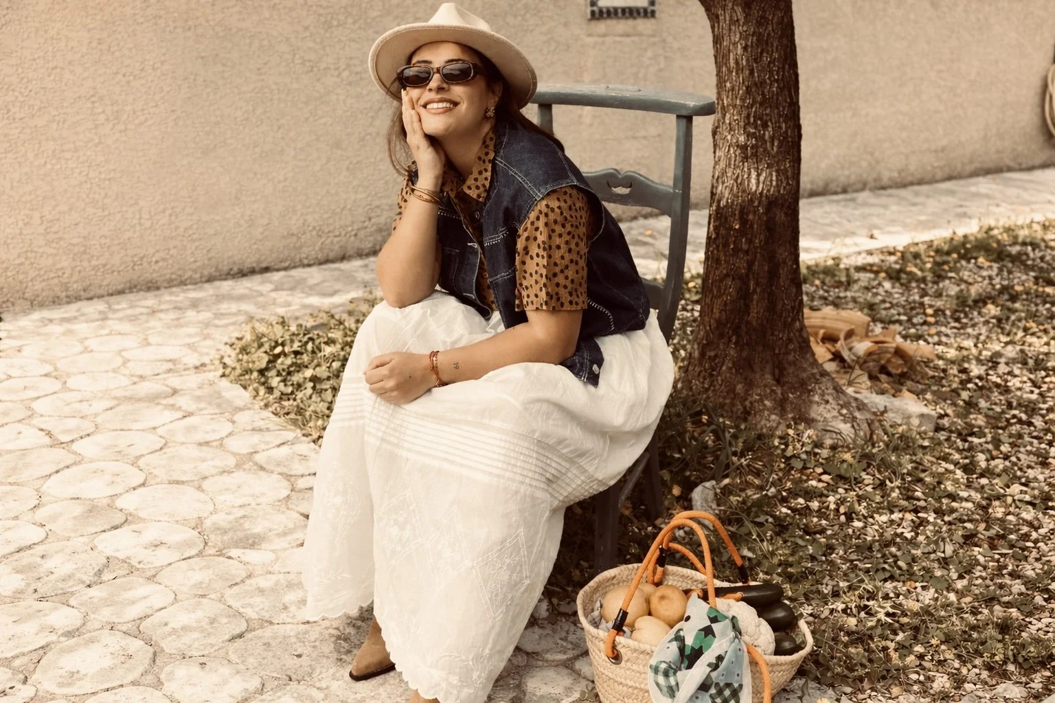 Une femme avec une jupe longue blanche en dentelle anglaise avec un petit haut à pois et un gilet sans manche en jeans 