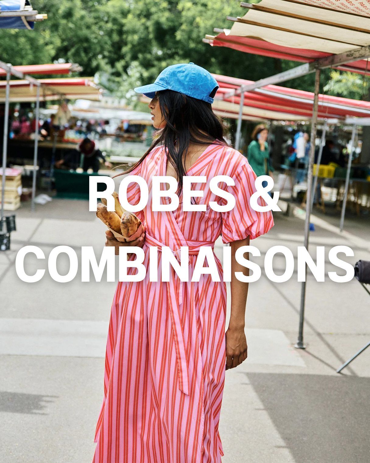 Une femme portant une robe à rayures rouges et blanches, un chapeau bleu, au marché en plein air, tenant un sandwich.