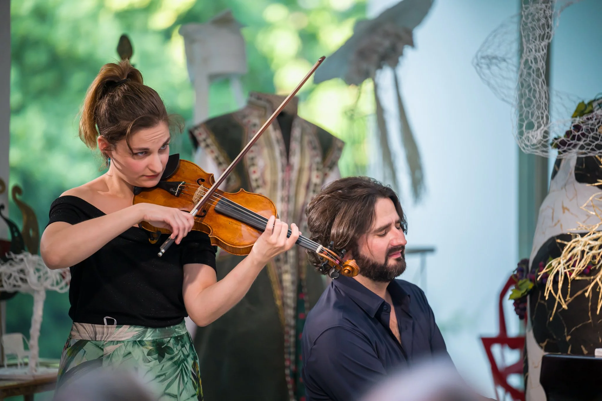 Une femme jouant du violon et un homme au piano dans un cadre intérieur avec des décorations artistiques.