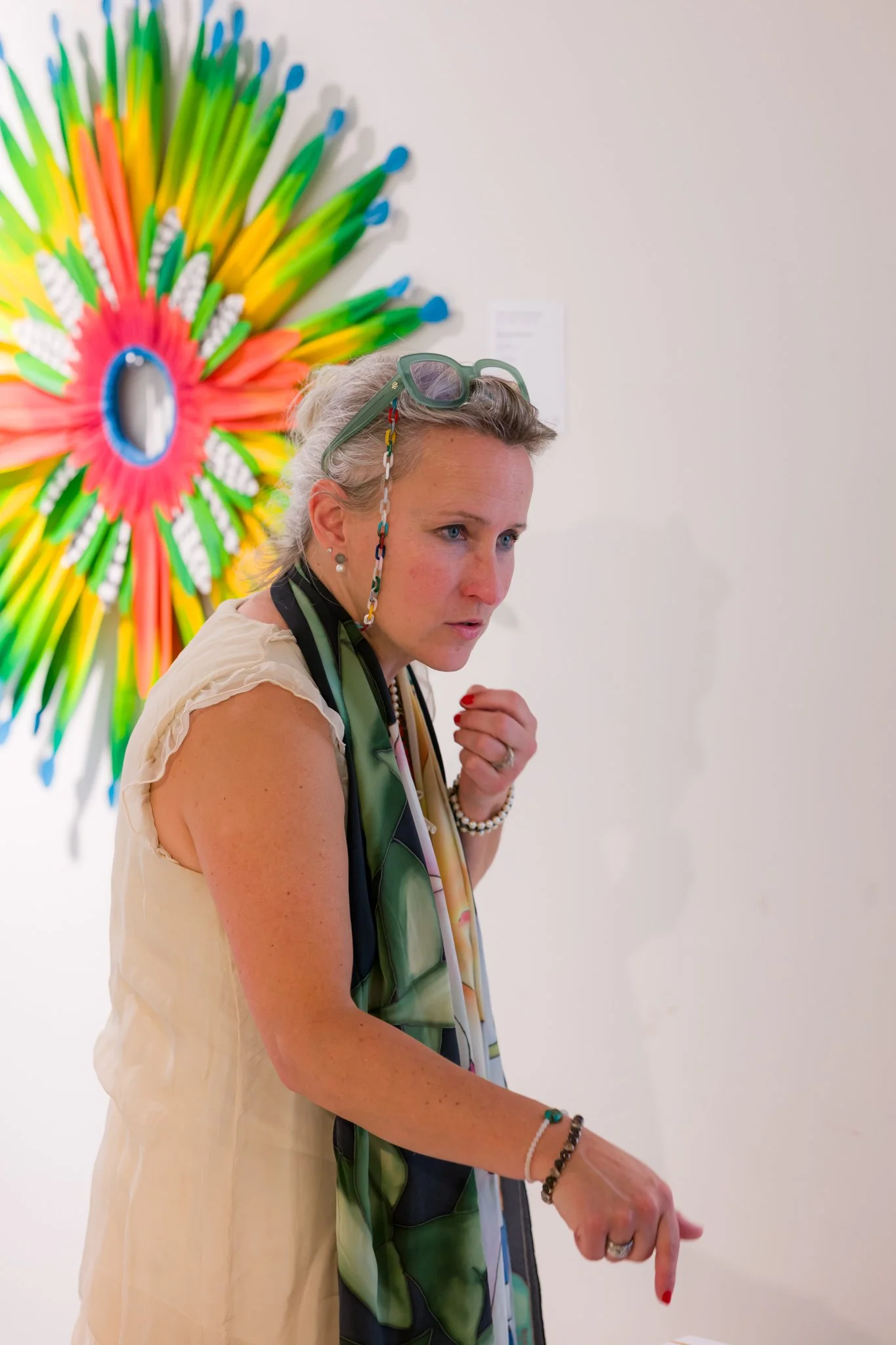 Femme regardant un tableau dans une galerie d'art, avec une œuvre colorée derrière elle.