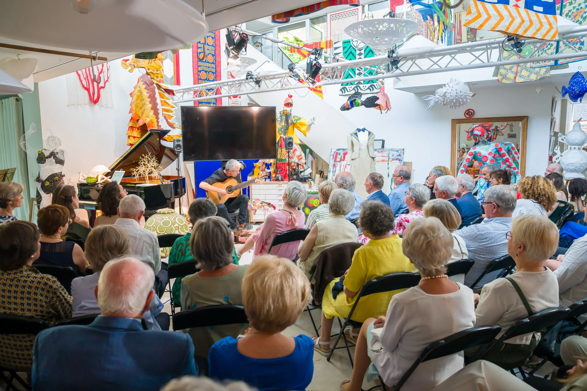 Spectacle musical avec un musicien jouant de la guitare devant un public assis dans une pièce décorée avec des œuvres d'art colorées