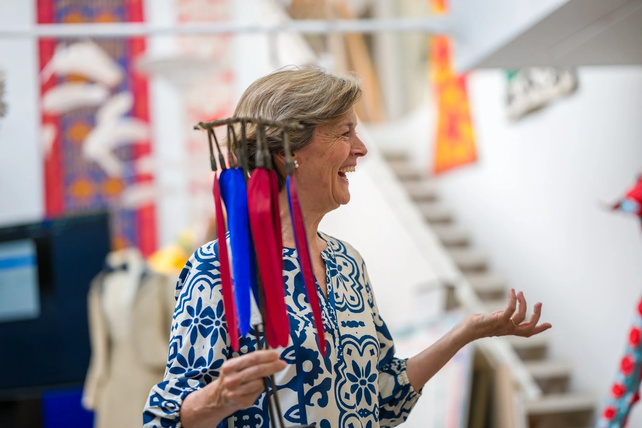 Une femme souriante avec des drapeaux colorés à la main dans un magasin de souvenirs.