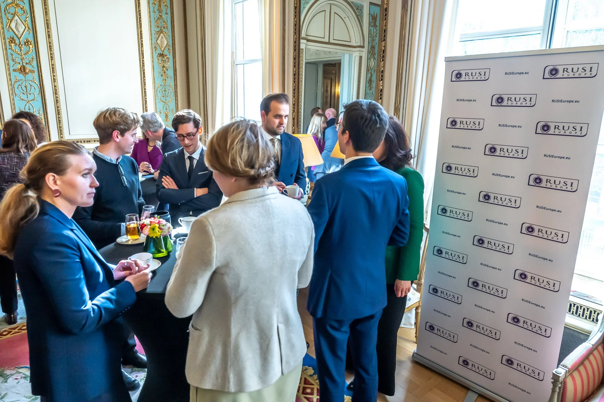 Group of people chatting at a formal event with a RUSI banner in the background.