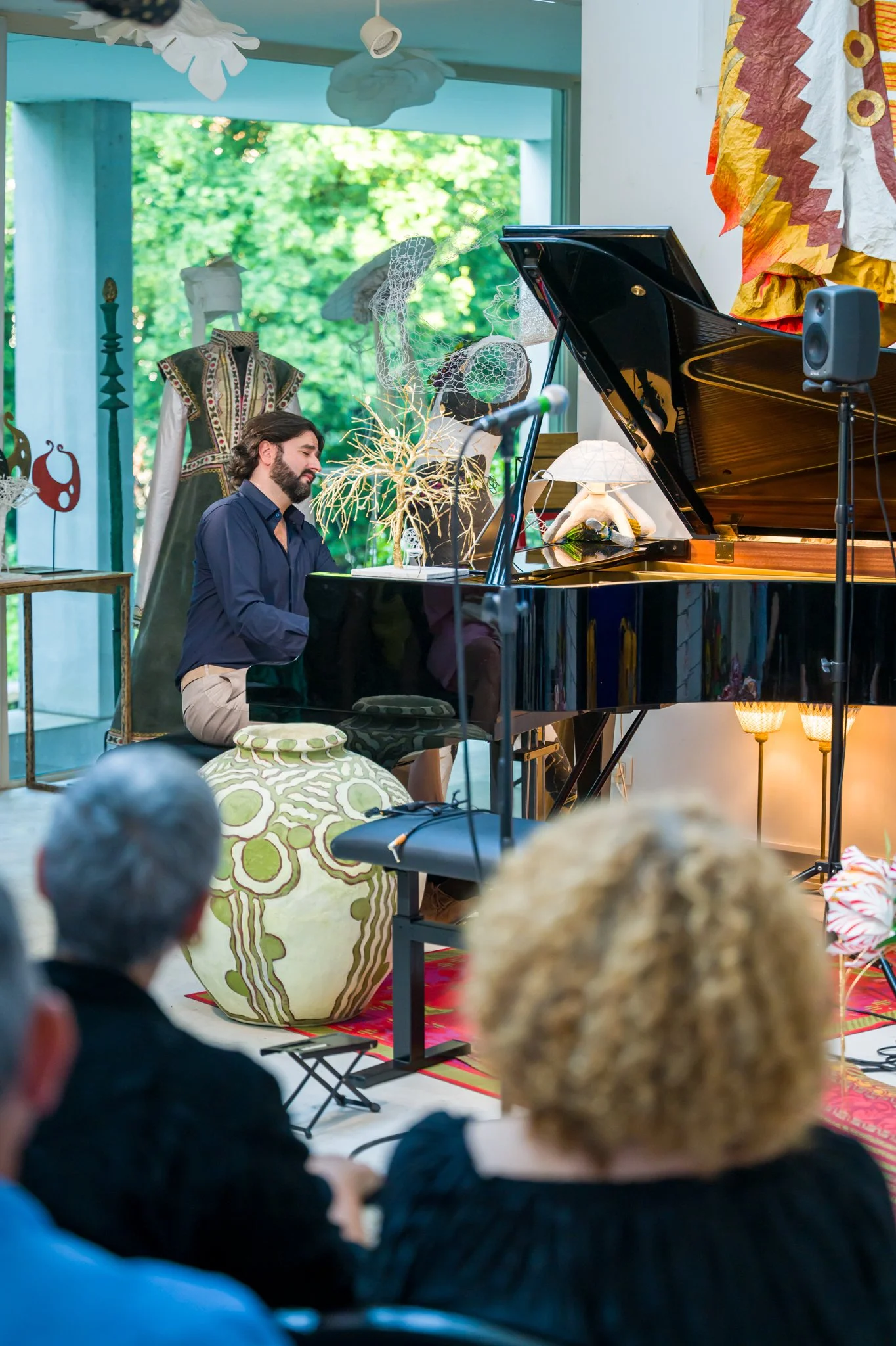 Un homme joue du piano lors d'un concert dans un espace décoré avec des œuvres d'art artisanales et un public regarde l'artiste.