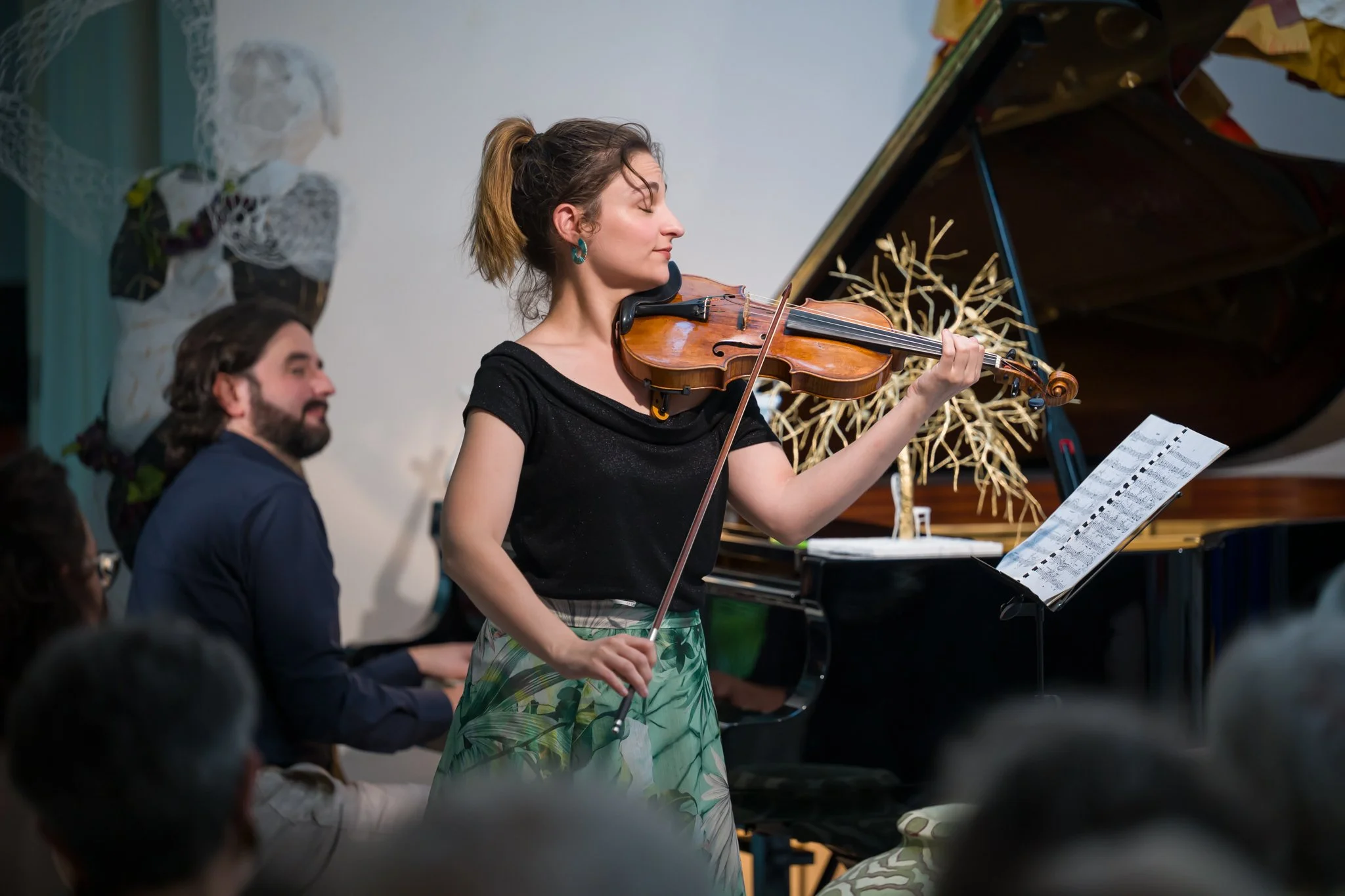 Femme jouant du violon lors d'une performance musicale, accompagnée d'un pianiste, dans une salle de concert.