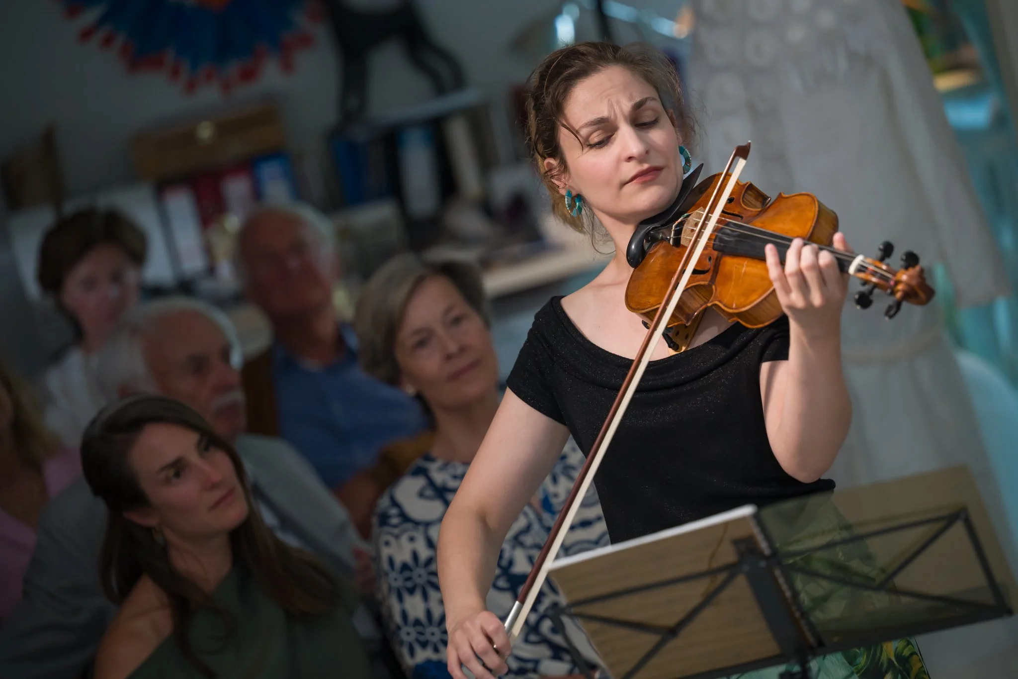 Jeune femme jouant du violon lors d'une performance, avec un public attentif en arrière-plan.