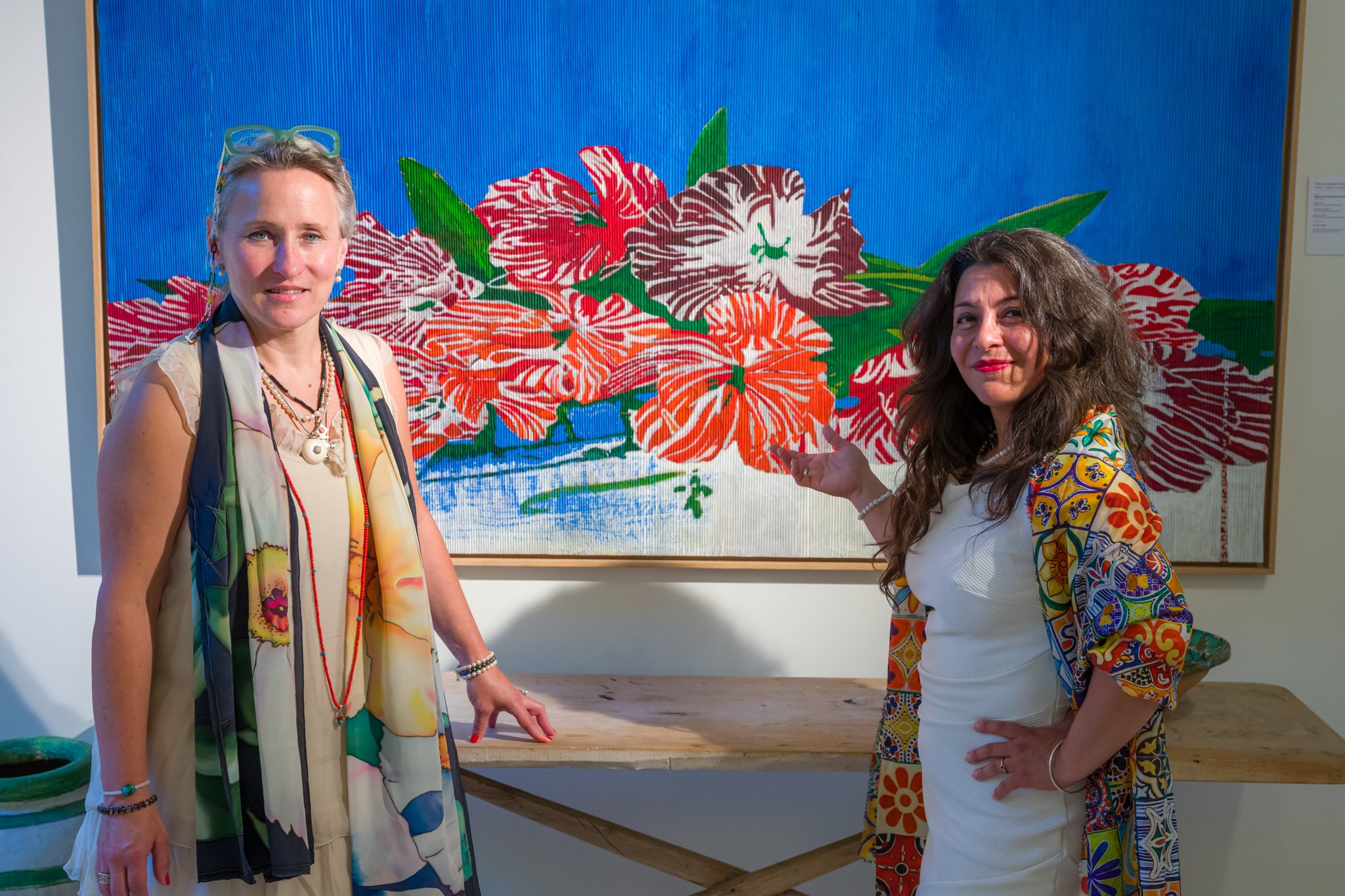 Deux femmes posant devant une peinture de fleurs colorées dans une galerie d'art.