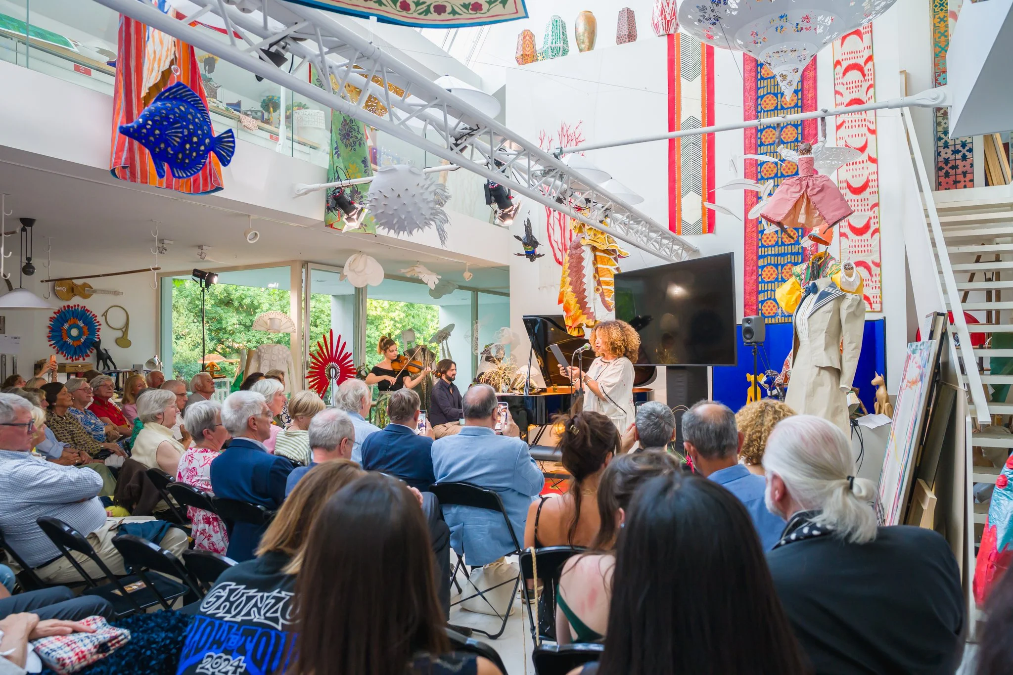 Une salle d'exposition ou un théâtre avec un groupe de personnes assises regardant une performance musicale, décorations colorées et objets d'art suspension