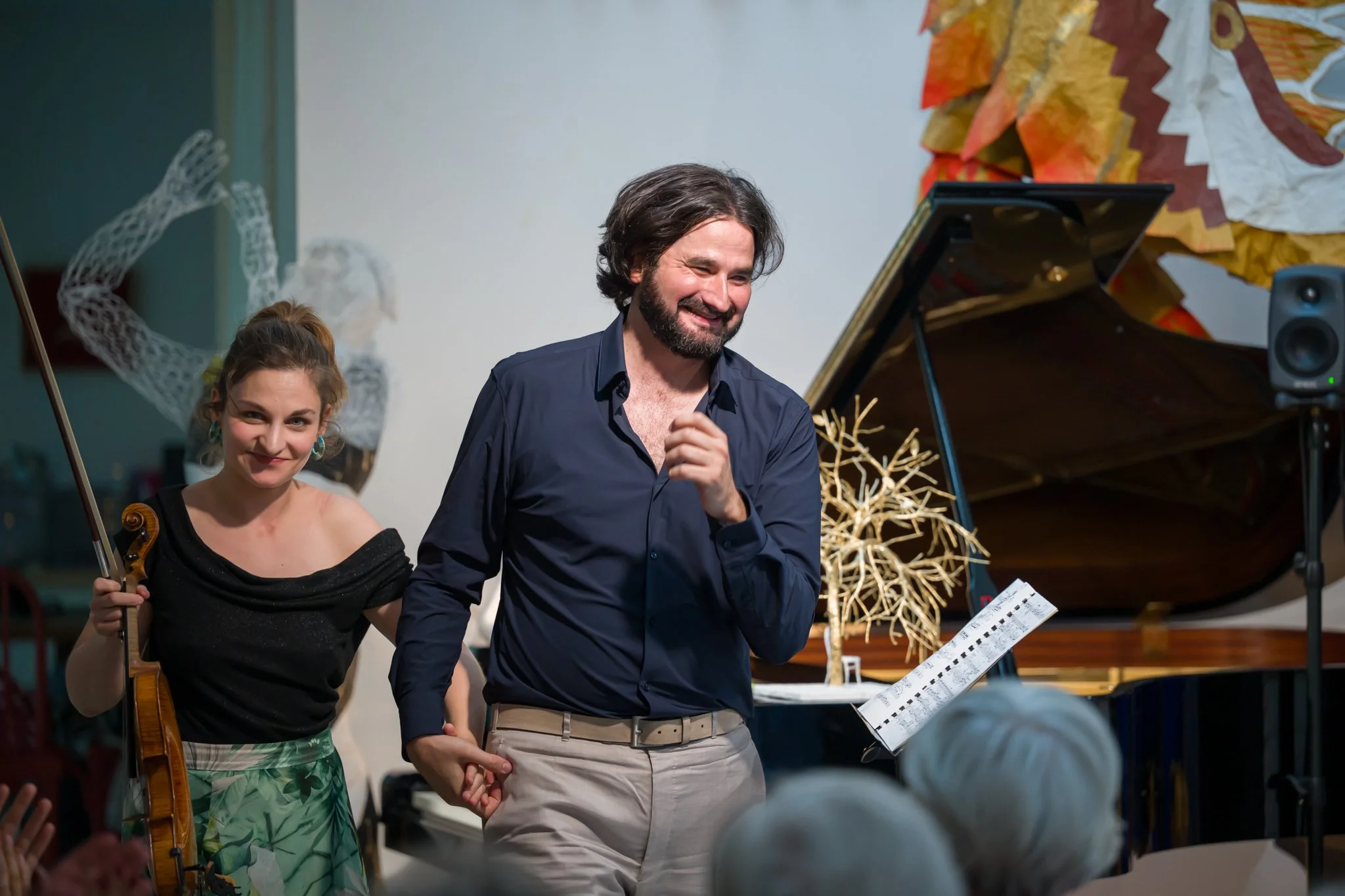 Un homme et une jeune femme se tiennent sur scène lors d'un concert ou d'une performance musicale. La jeune femme tient un violon et sourit, tandis que l'homme semble être le musicien ou le chanteur et affiche un sourire. Un concert ou une performanc