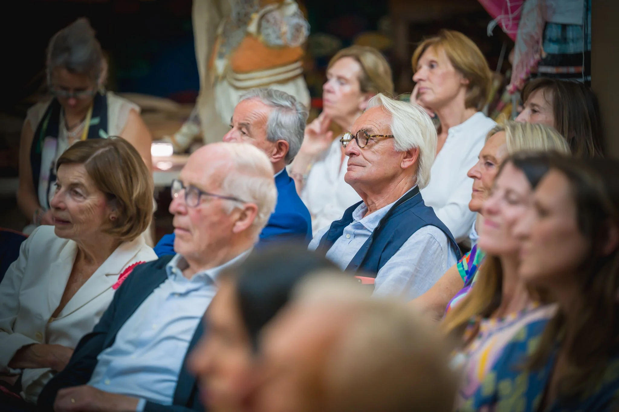 Groupe de personnes âgées assises en salle, écoutant attentivement lors d'un événement ou d'une conférence.