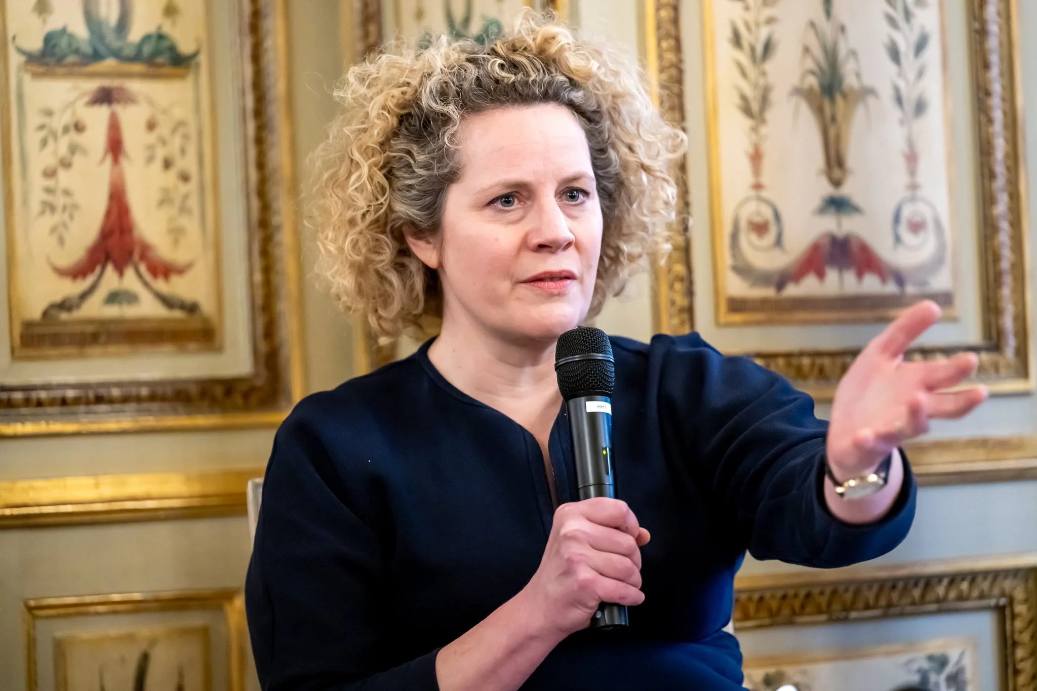 Woman with microphone talking in a decorated room.