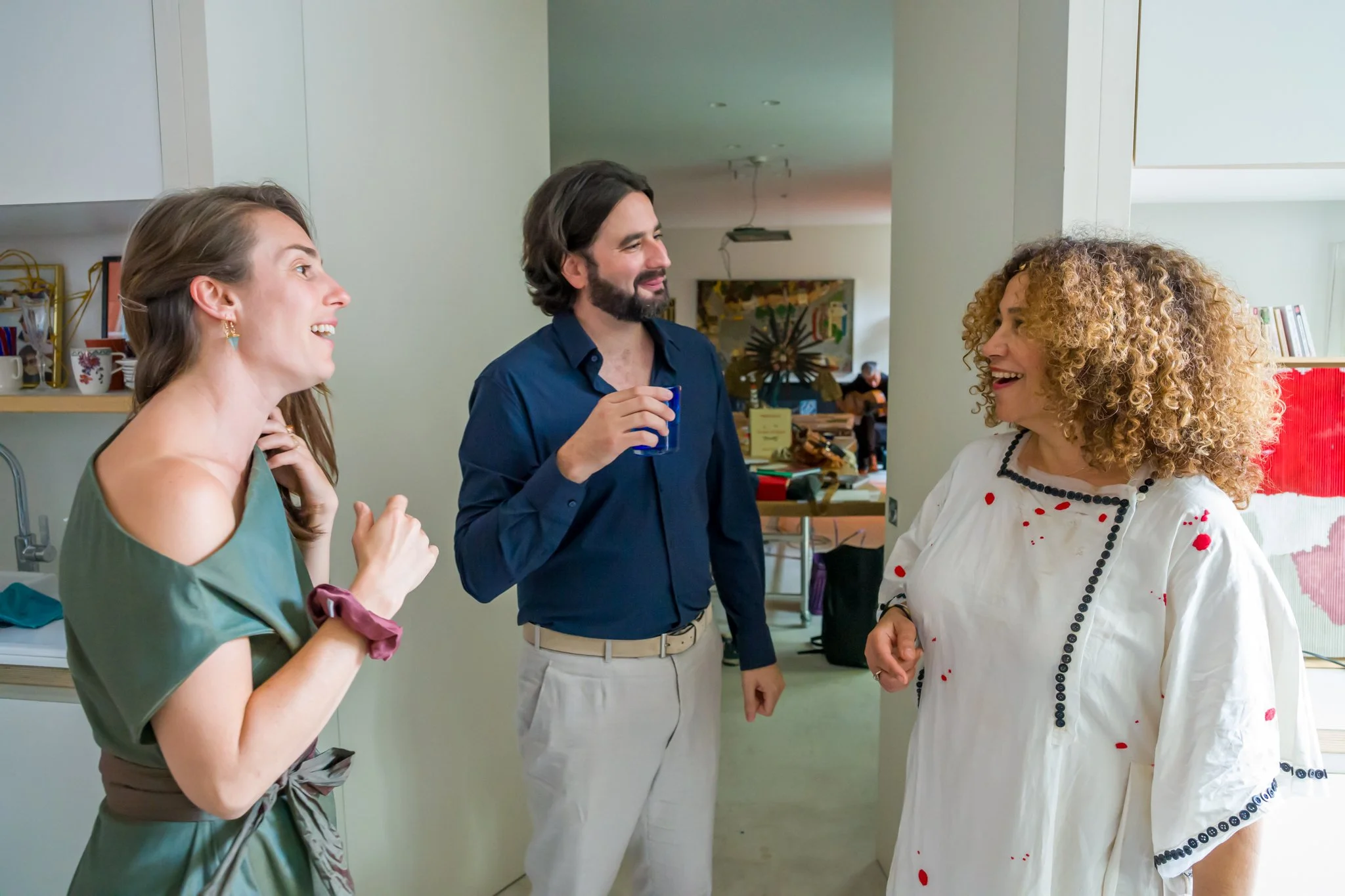 Trois personnes souriantes, deux femmes et un homme, discutent dans une cuisine ou un salon lumineux.