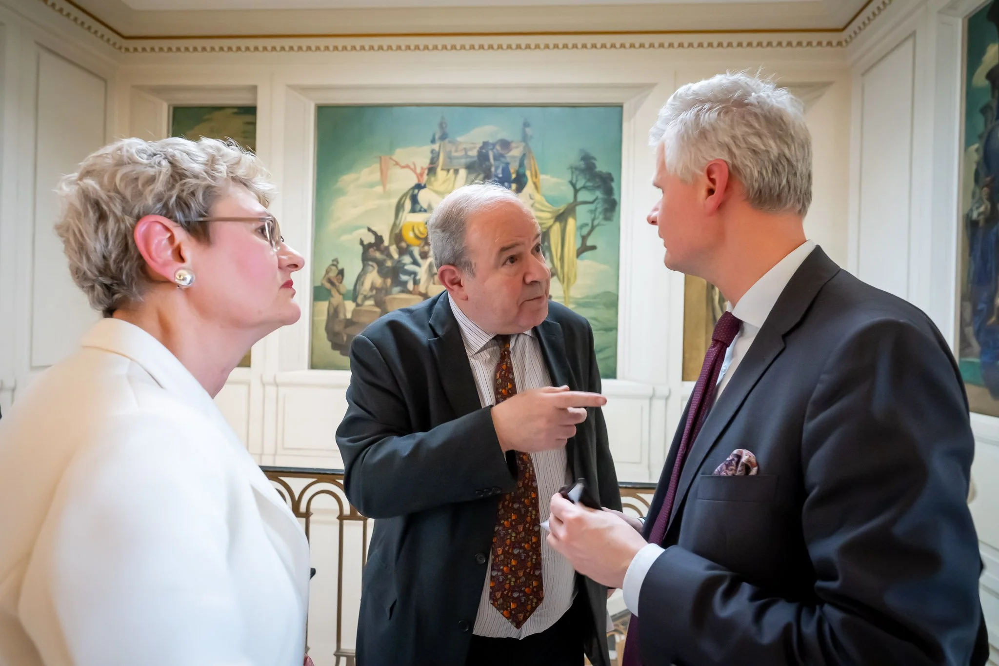 Three people in costume and animated discussion in a room decorated with large murals.