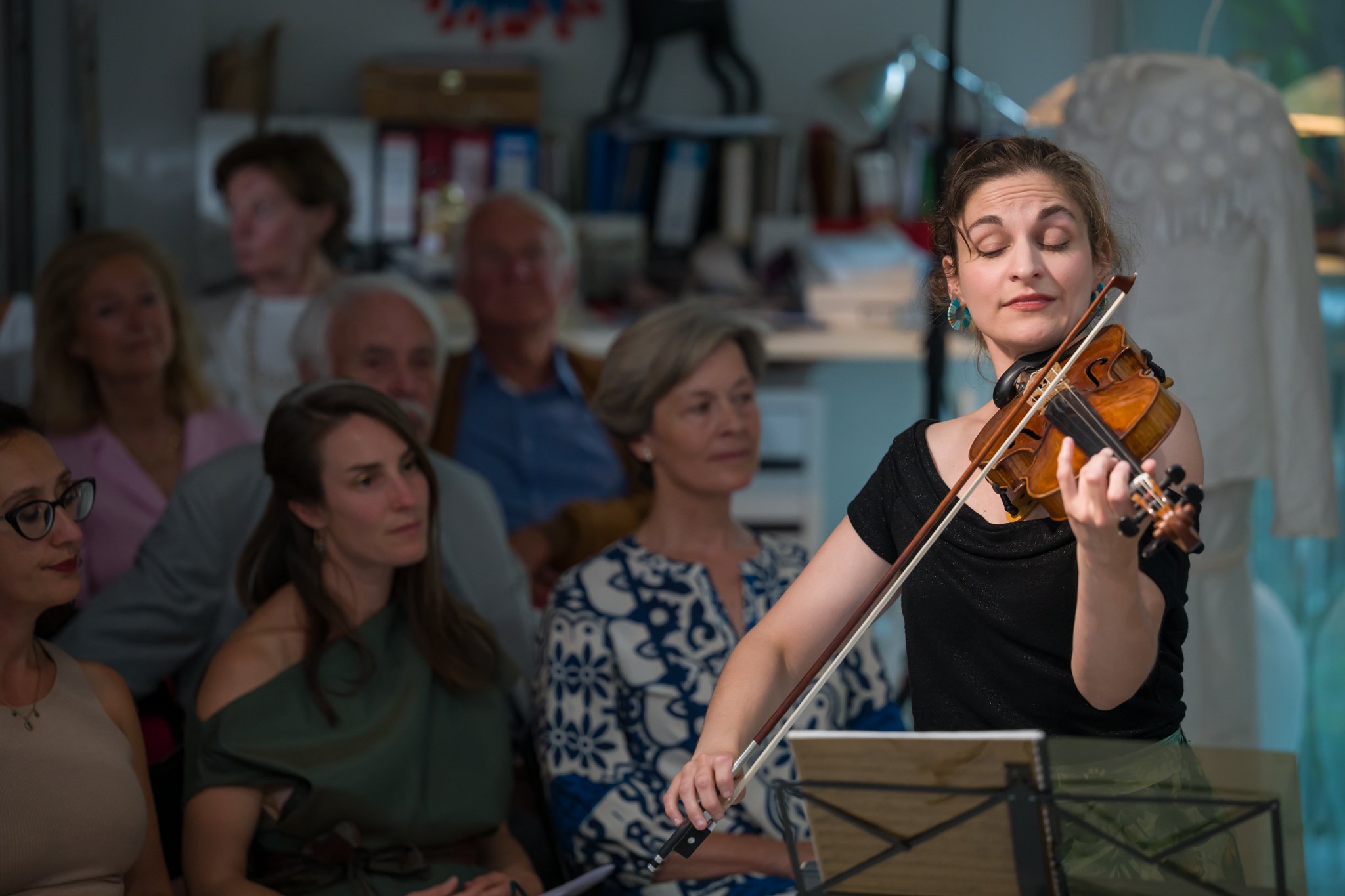 Jeune femme jouant du violon lors d'une performance devant un public dans un intérieur.