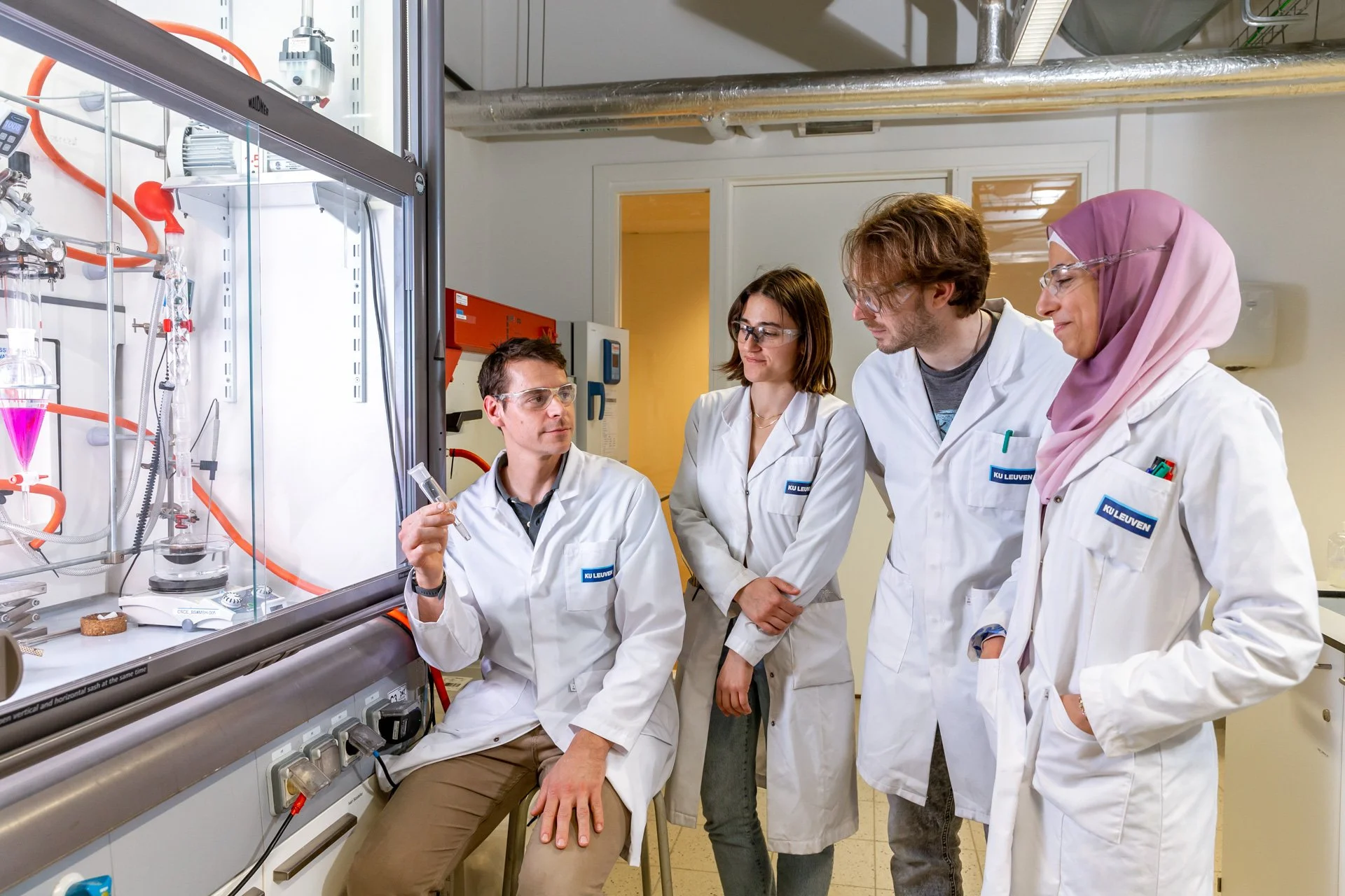 Professional photograph of a team of four researchers in a laboratory in front of a laminar flow hood taken by an ISOWAY pro photographer.