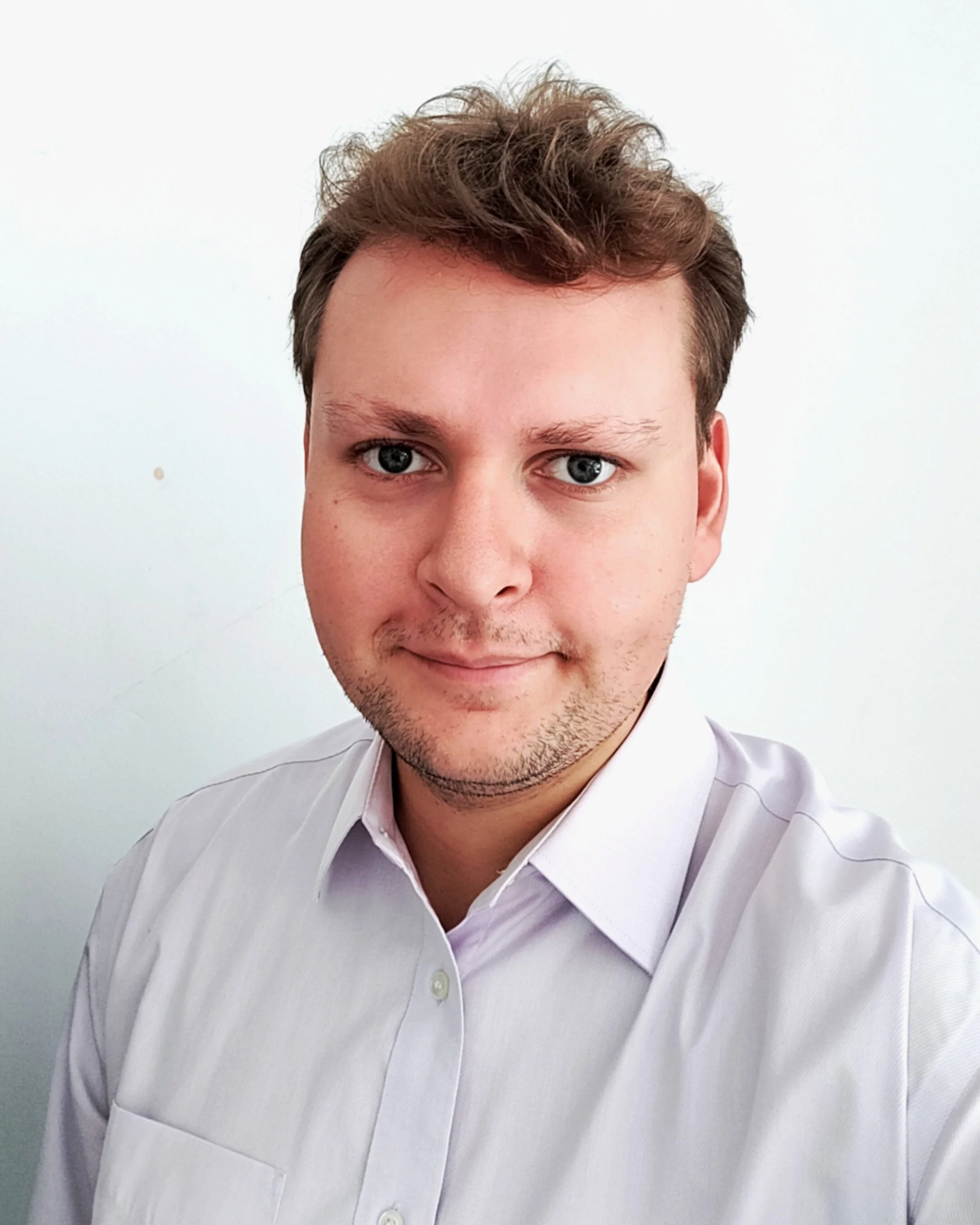 Person with short hair in a light-colored dress shirt, smiling at the camera.