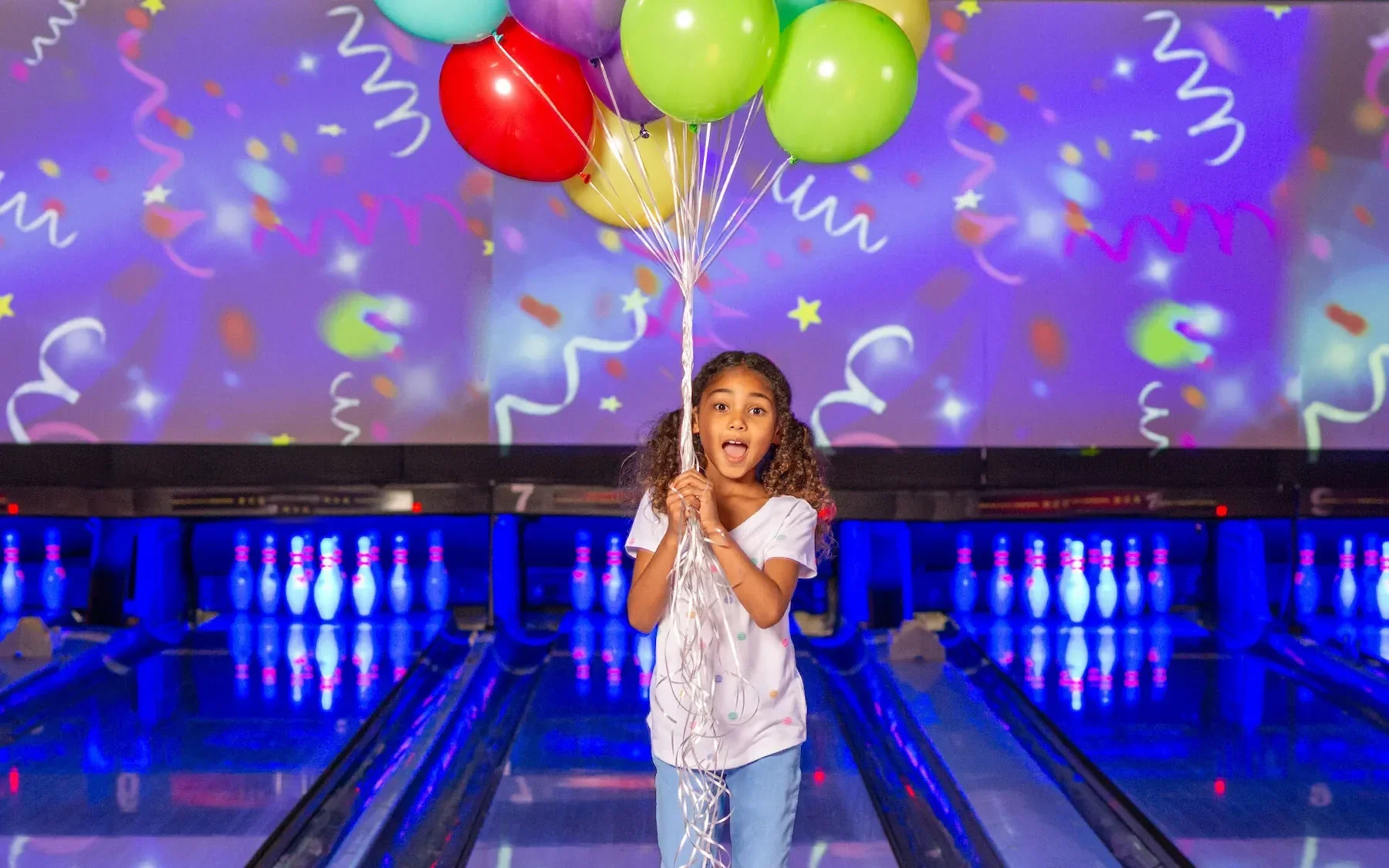 People at a bowling alley with three bowling lanes, some individuals preparing to bowl, others watching and socializing.
