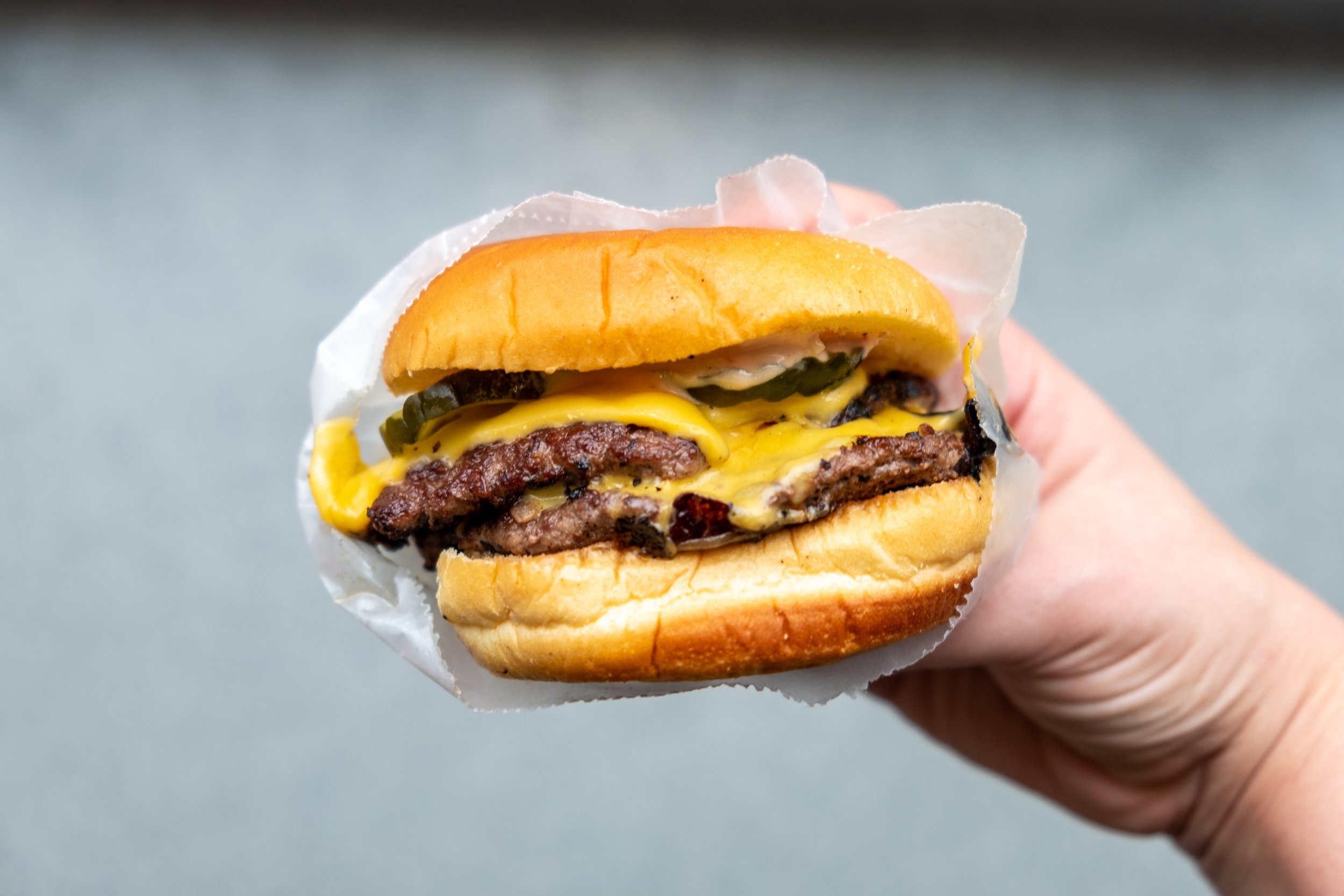  hand holding a double cheeseburger against a grey background 