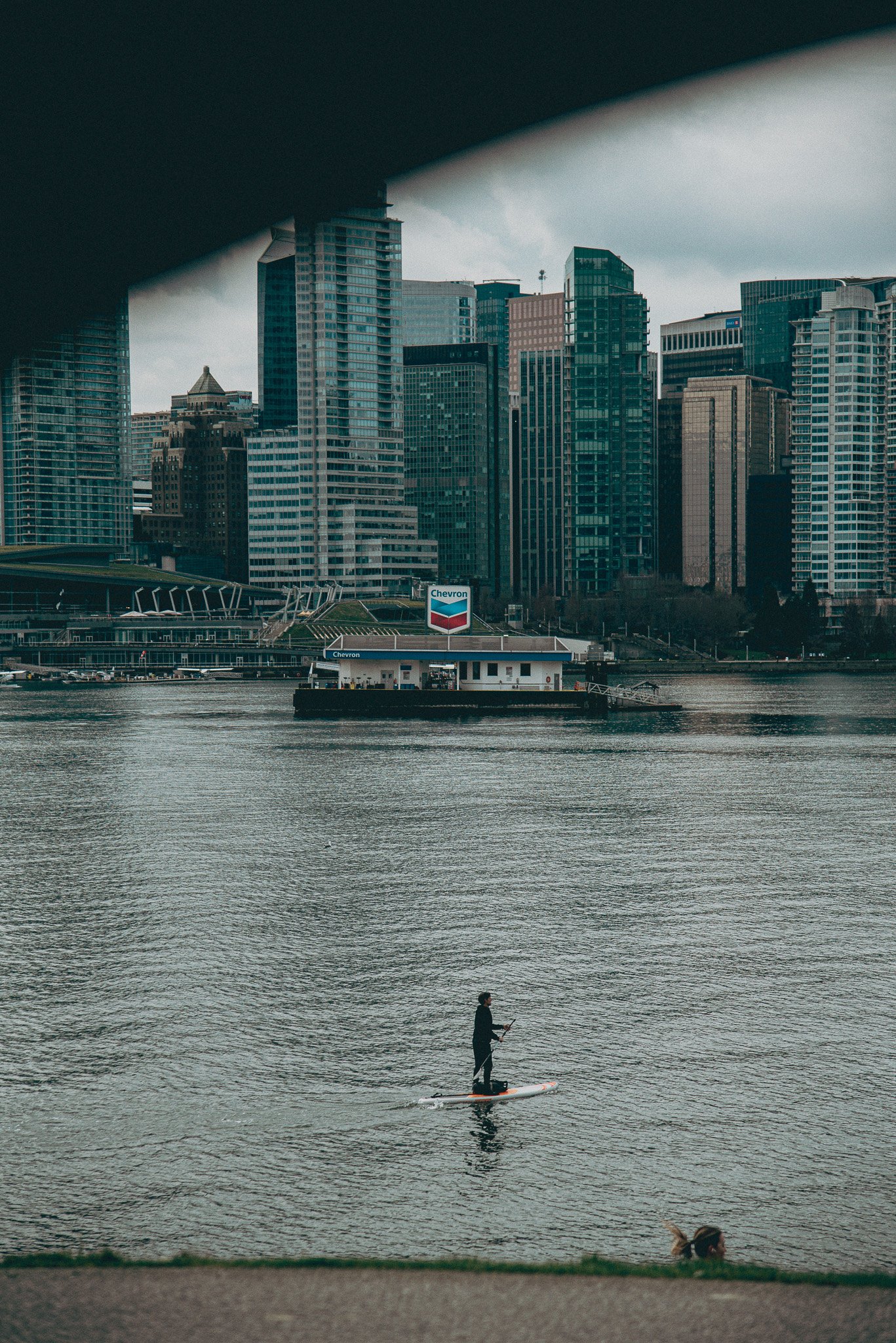 A man paddle boards in the cold Vancouver water with the skyline in the background.