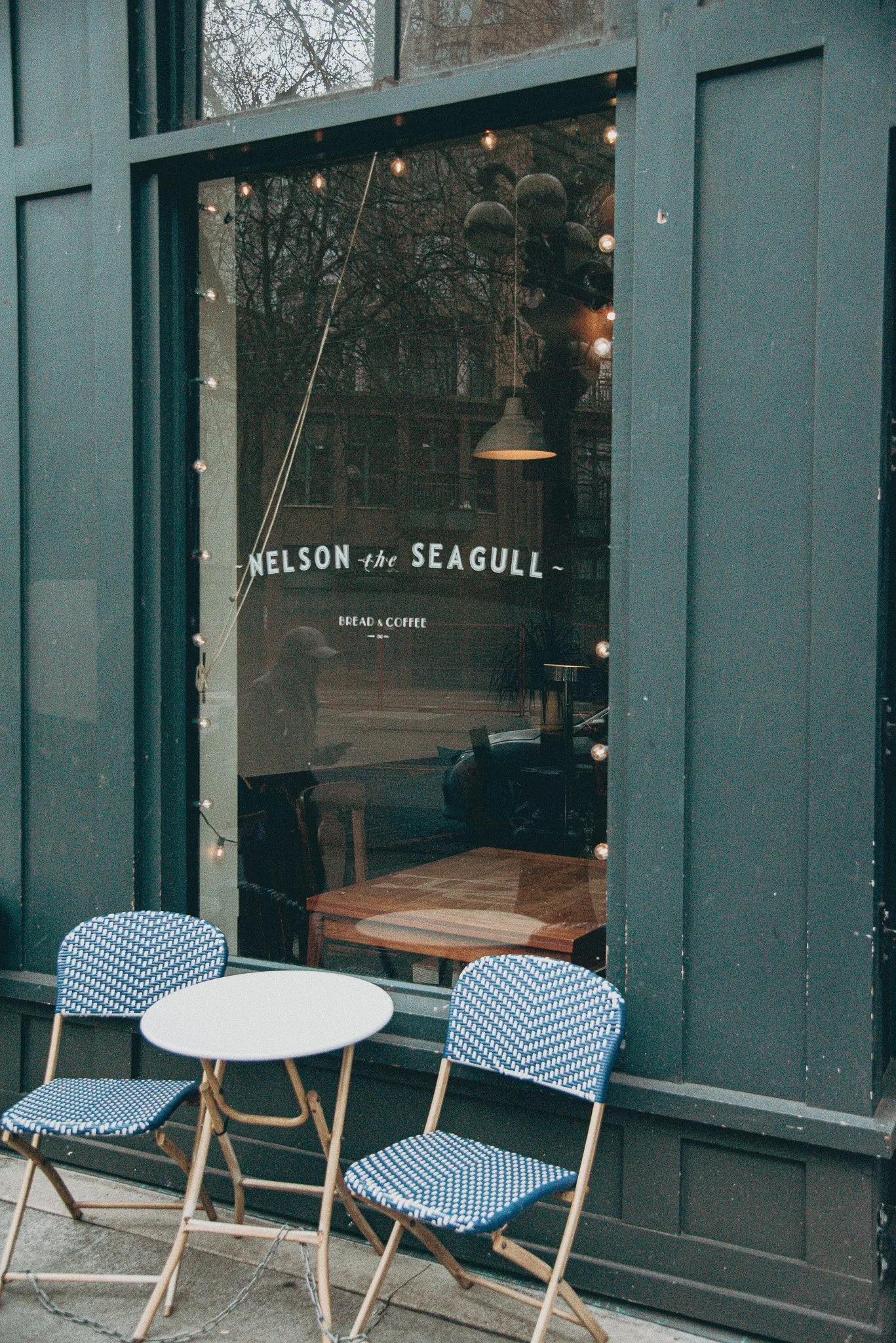 Two cafe chairs sit outside of a well-known bakery and Vancouver, BC called Nelson the Seagull