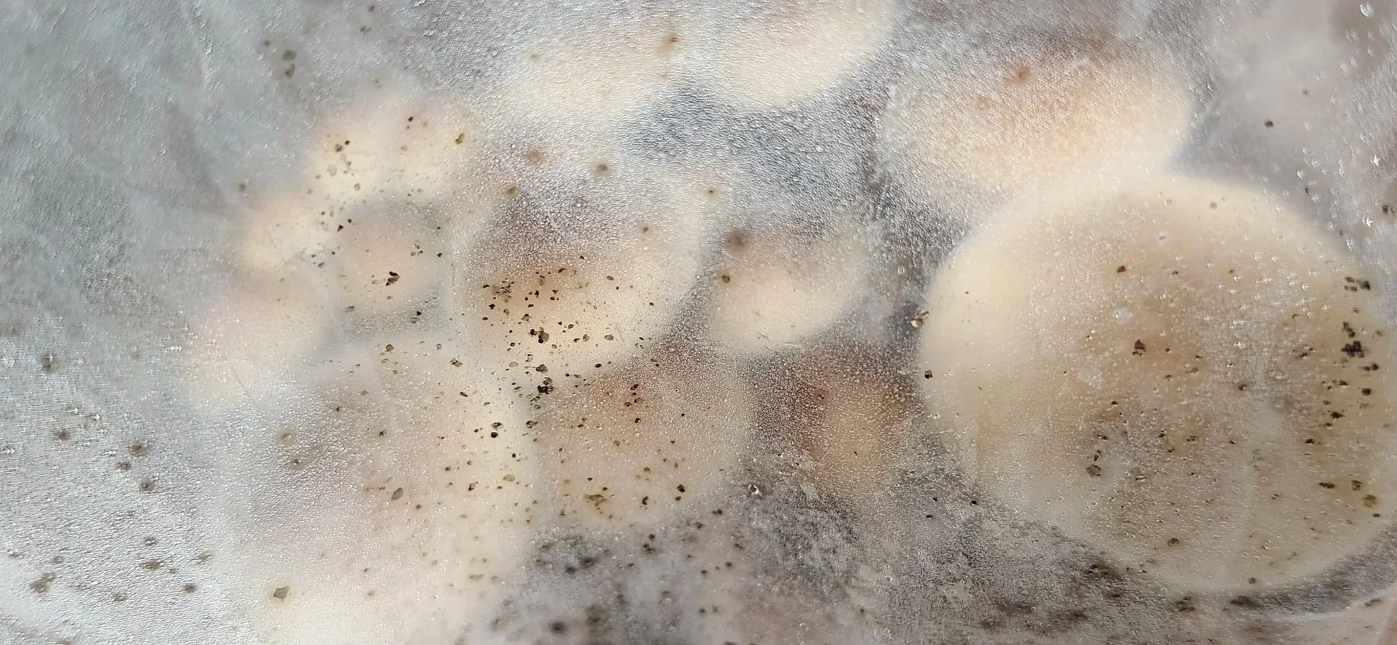 A close-up view of a metal surface with condensation, showing water droplets, black specks, and smudges.