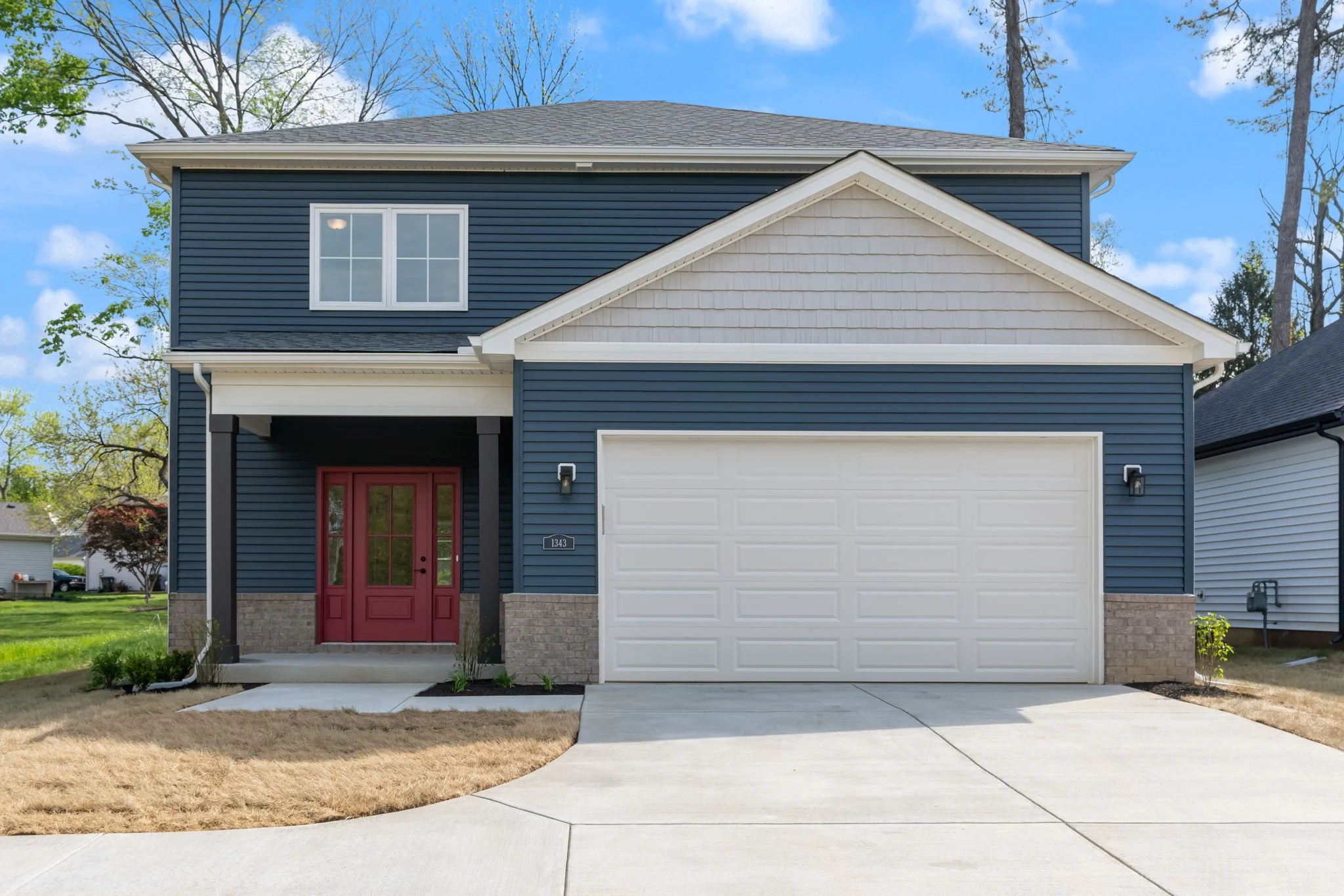 Two-story house with blue siding, white trim, and a red front door, with a grey garage door and a concrete driveway.