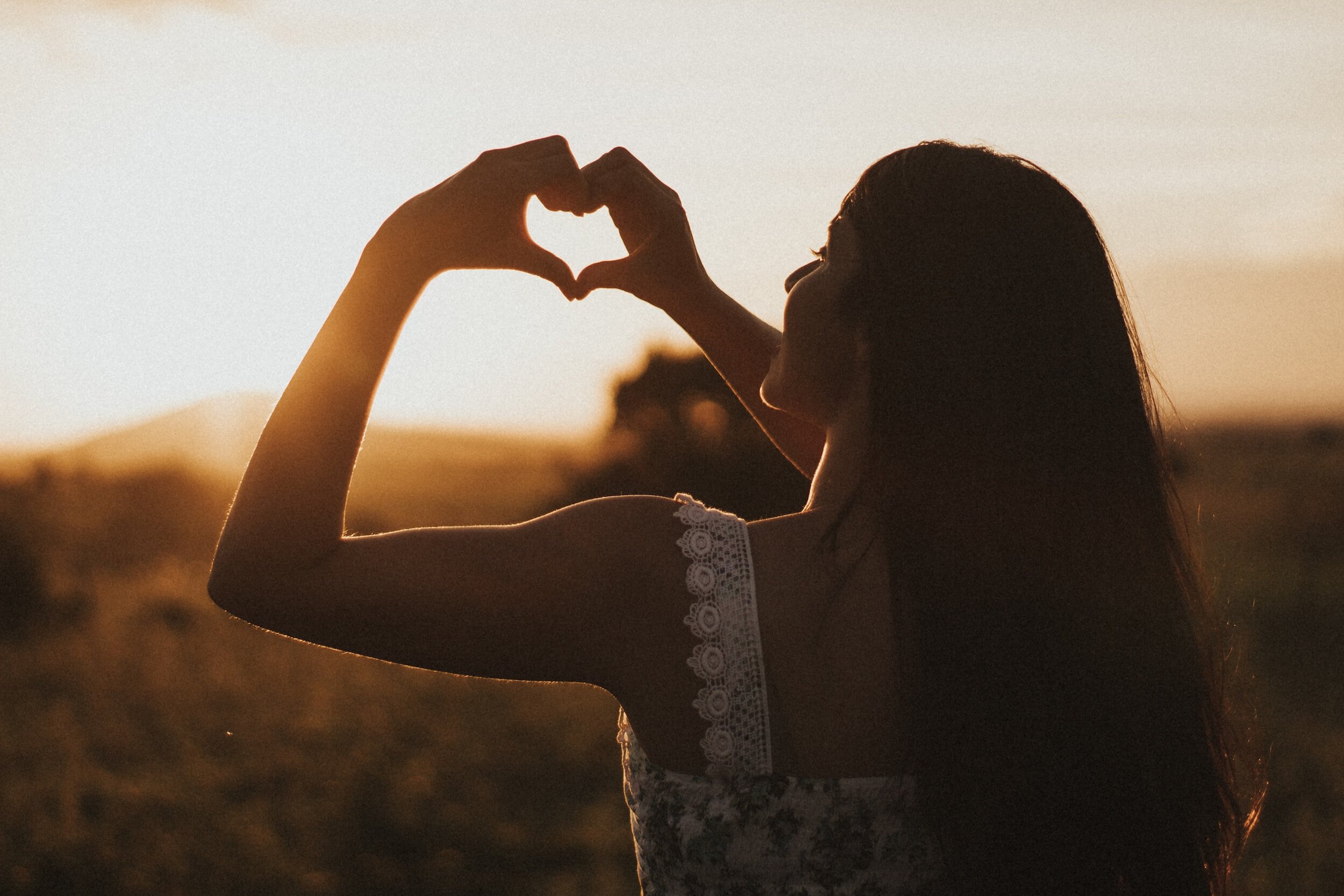 Silhouette of a woman making a heart shape with her hands against a sunset background.