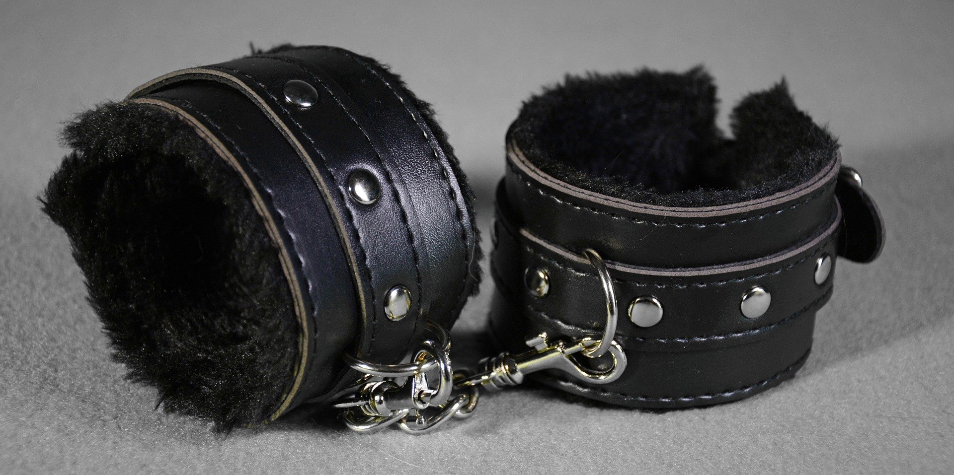 Pair of black padded leather cuffs connected by a short metal chain.