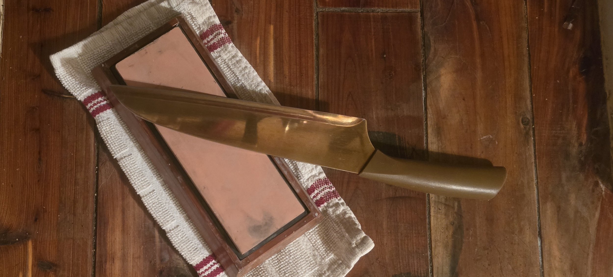 Golden kitchen knife resting across sharpening stones on a striped towel atop a wooden counter.