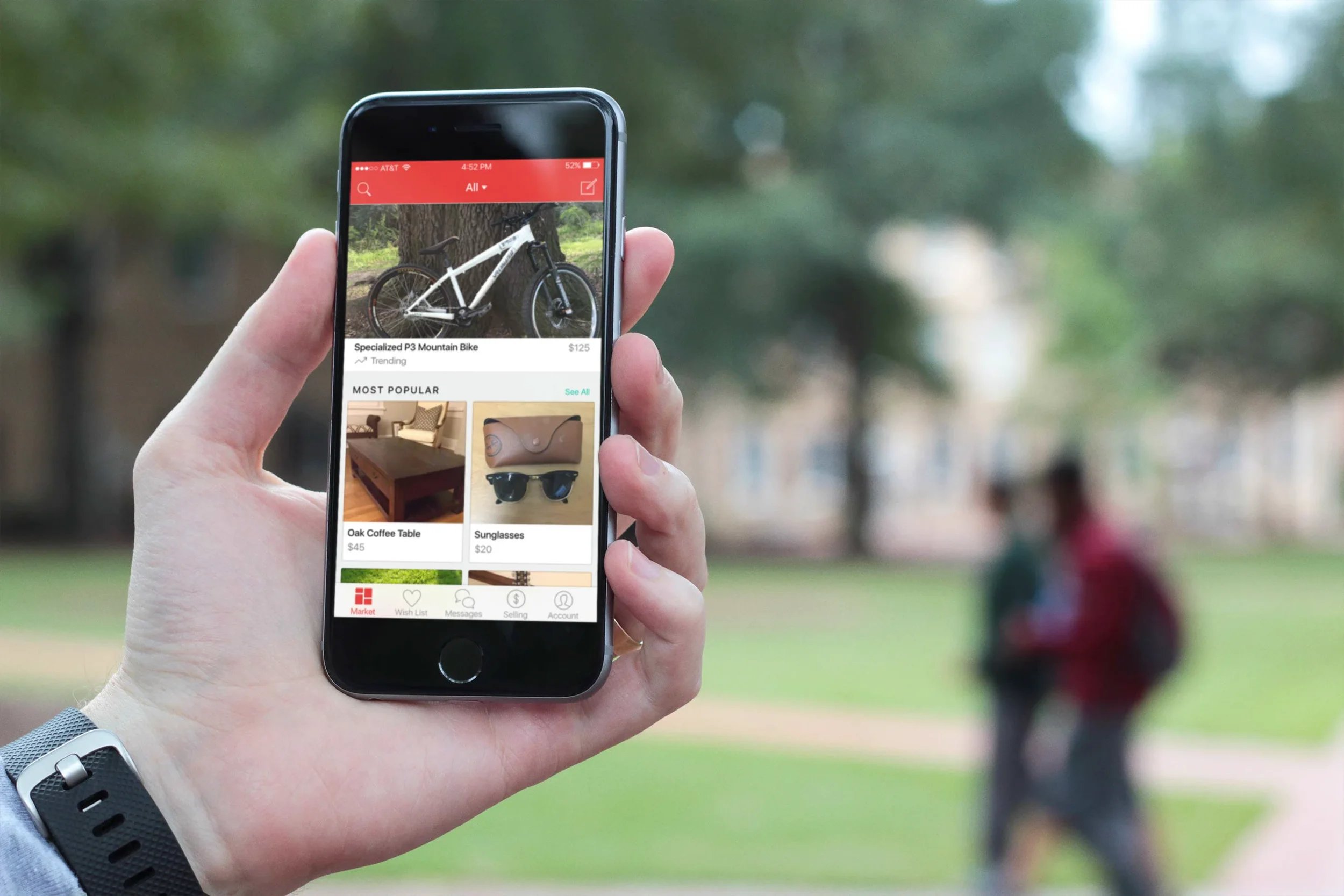 Person holding up iPhone displaying a red-branded marketplace application with a bike, coffee table, and sunglasses for sale