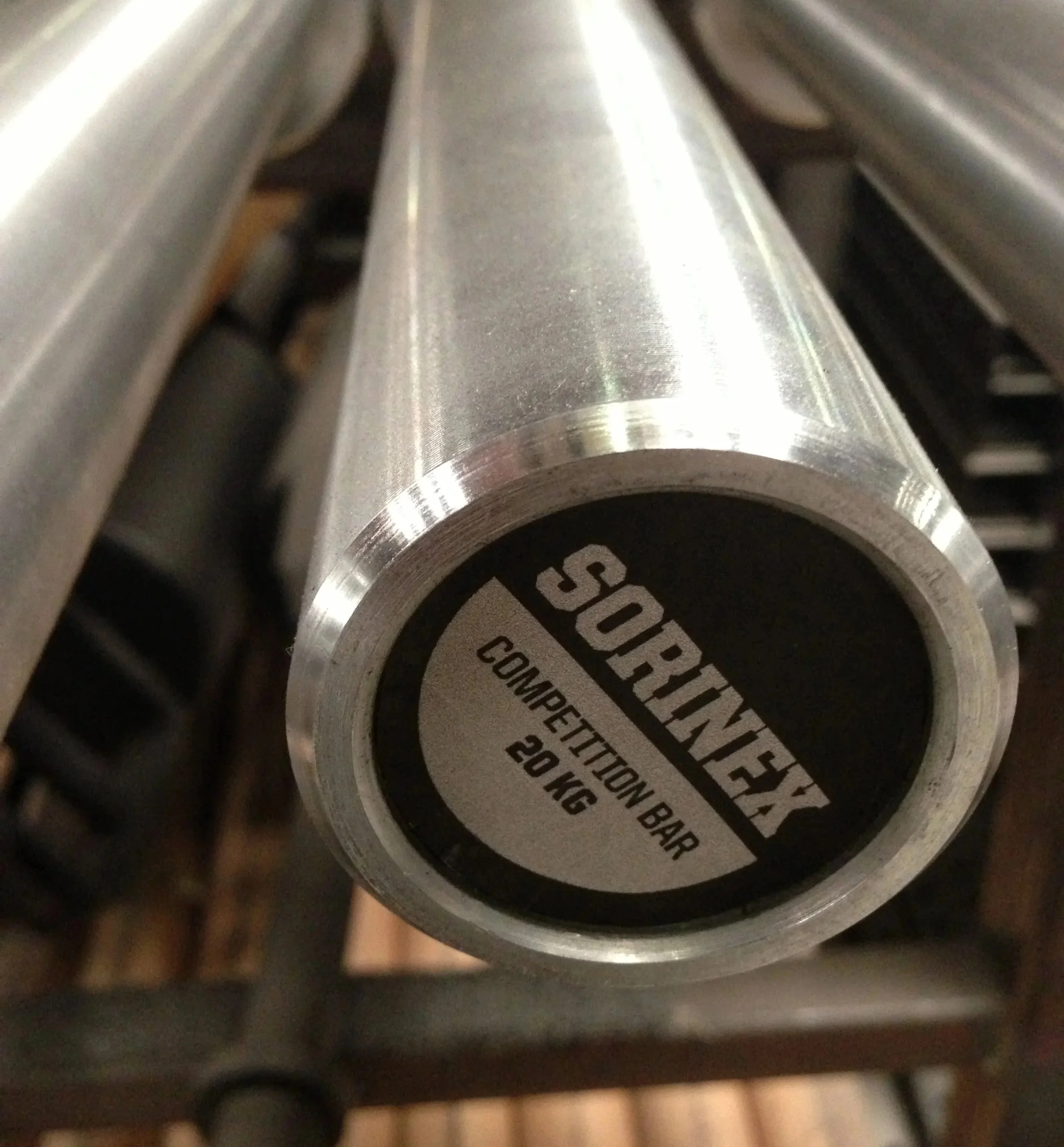 Close-up of a silver metal barbells with a black sticker on one end that reads "SORINEX COMPETITION BAR 20 KG."