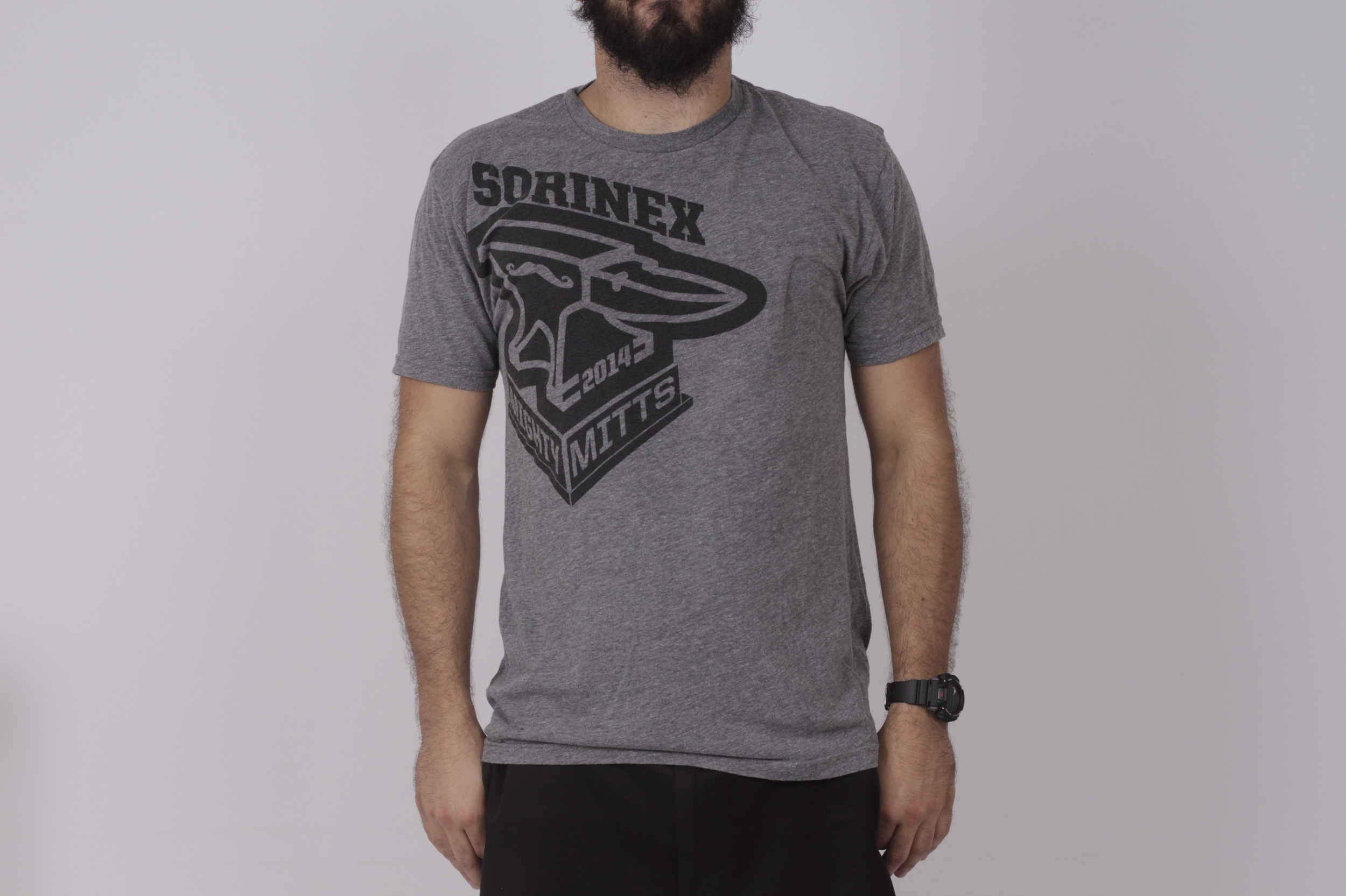 A man wearing a gray Mighty Mitts T-shirt with a black graphic design of anvil and text, standing against a plain light-colored background.