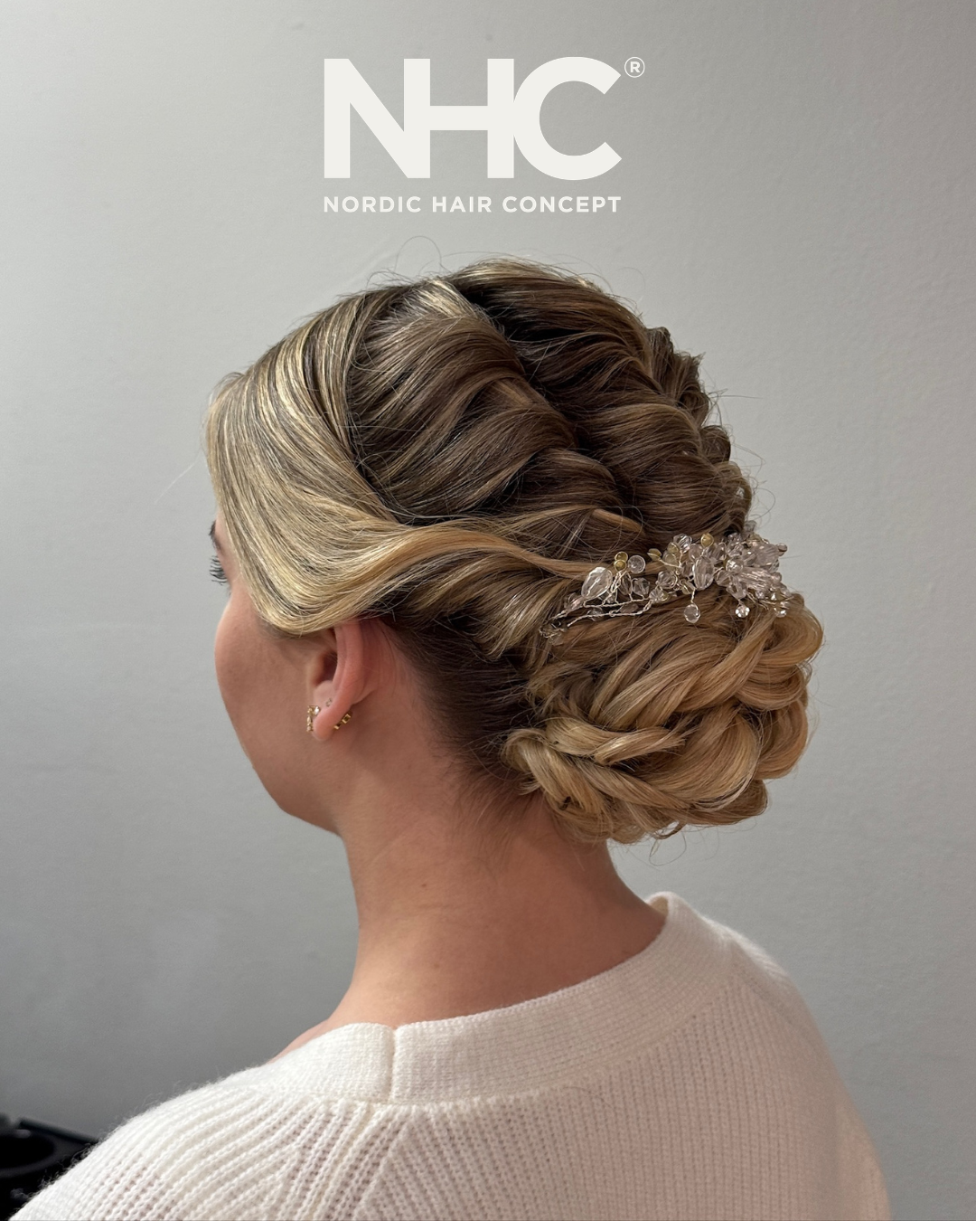 En kvinde med en elegant, flettet opadvokset frisyr dekorert med en klar, mimetisk håraccessory, set fra bagsiden.