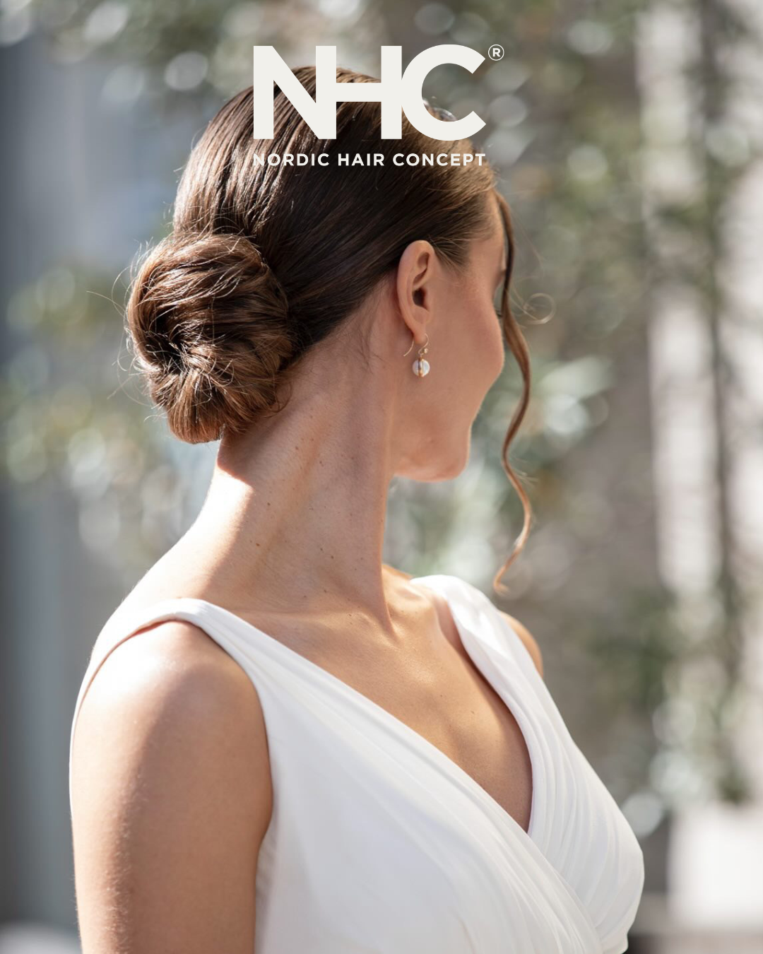 Kvinde med opadv generallys hår i en twist, der bærer en hvid kjole og øreringe, set fra siden mod en naturbaggrund.