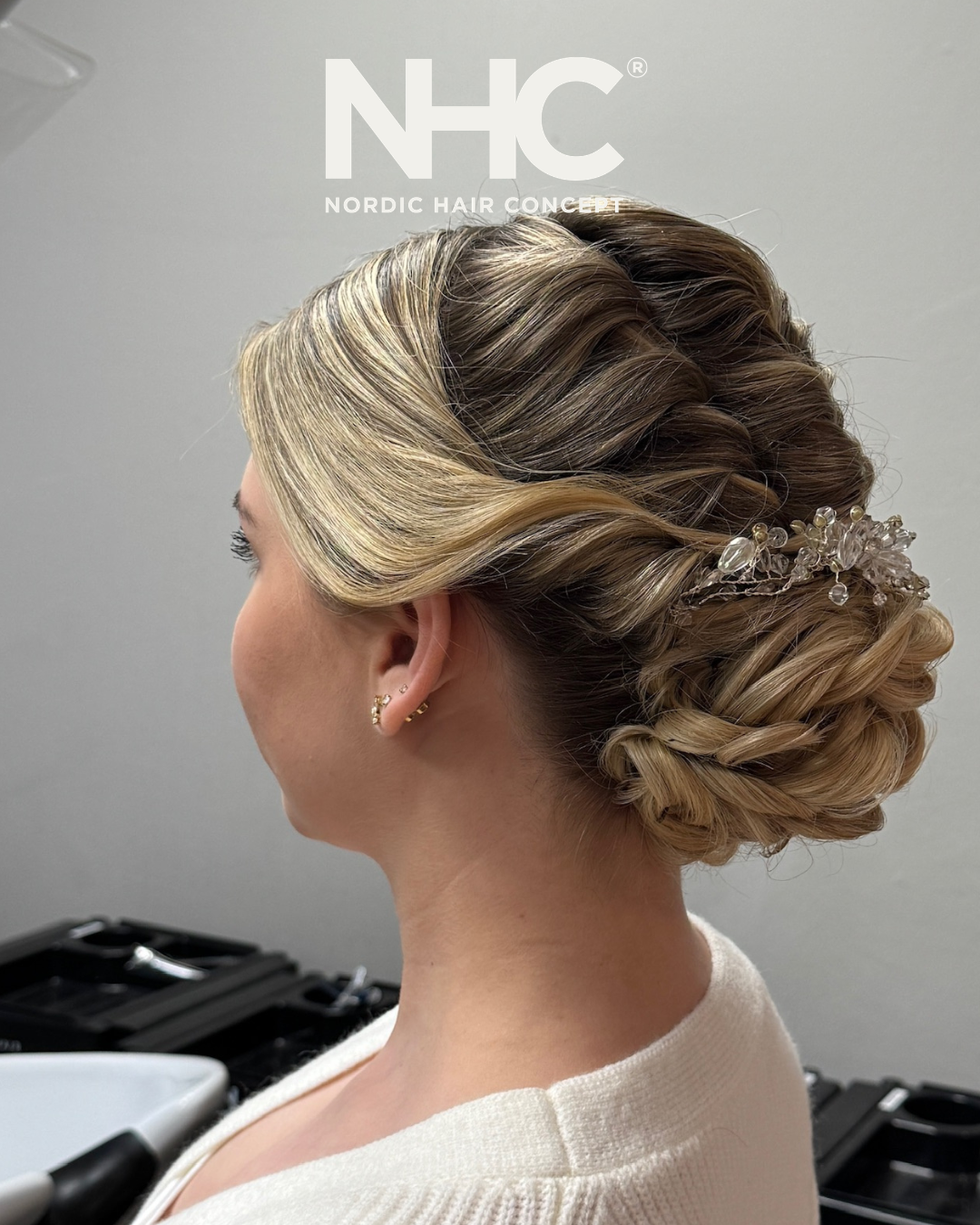 Elegant opsetning af en kvindes hår med bølger og en hårnål dekoreret med perler, set fra siden, i en frisørsalon.