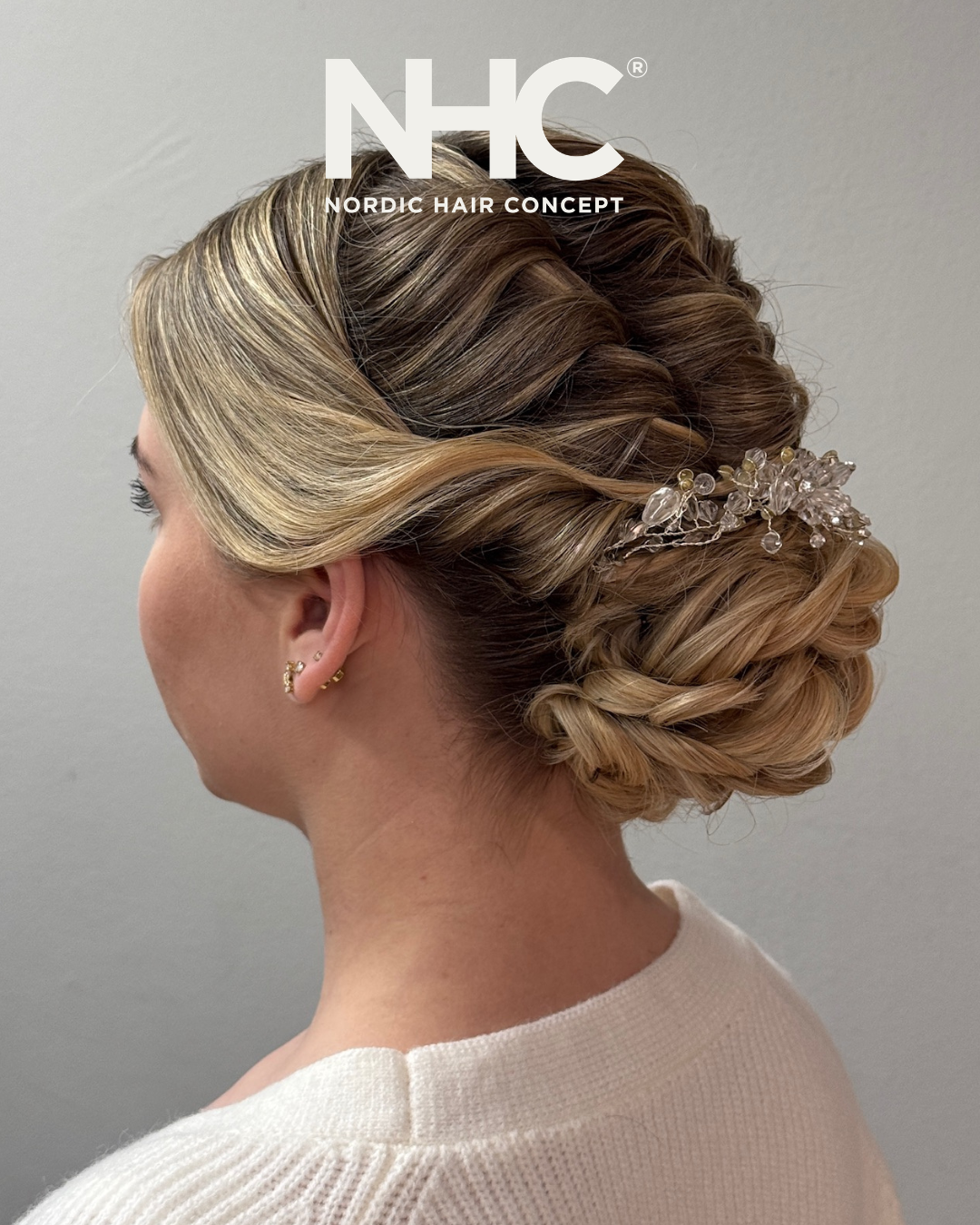 En sideprofilbilled af en kvinde med en elegant oppyntet, flettet håropsætning med en dekorativ håraccessory med perler og krystaller.