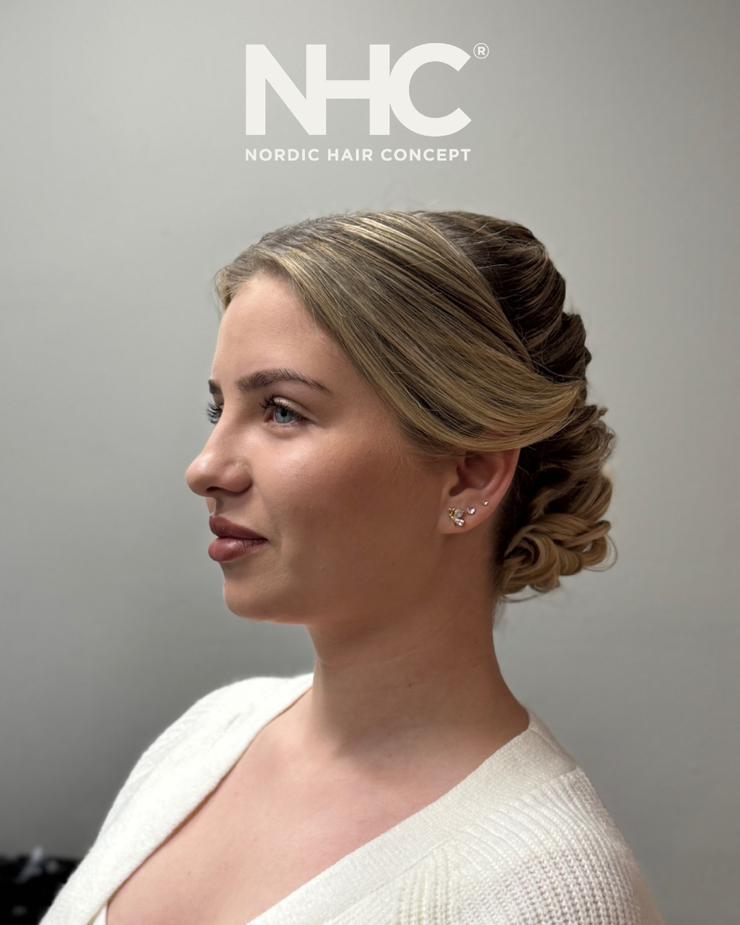 Profilbillede af en kvinde med stylet lyst hår, der har små øreringe, iført en cremefarvet sweater.