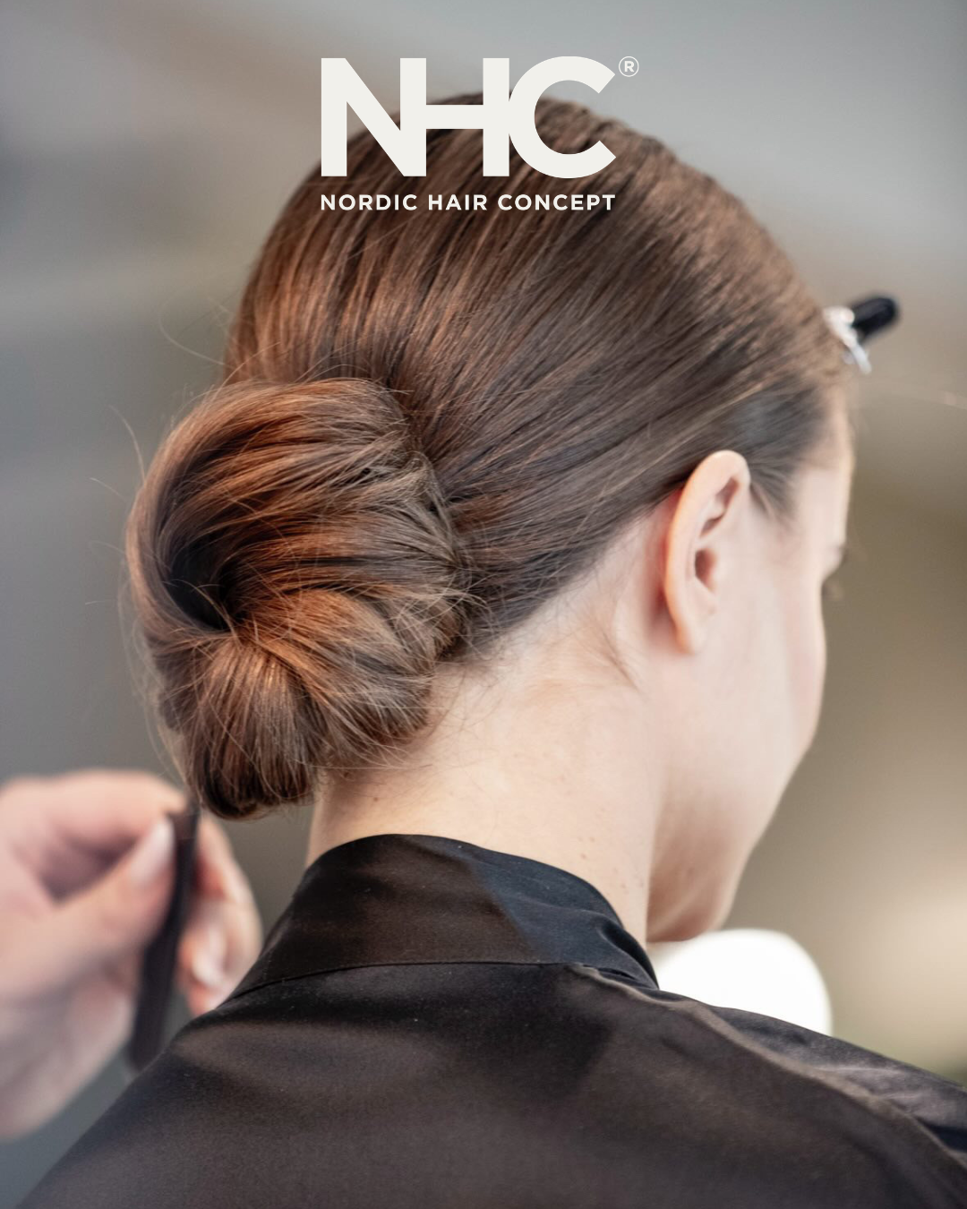 En kvinde med opmagset hår i en elegant knold, mens en frisør arbejder med hendes hår.