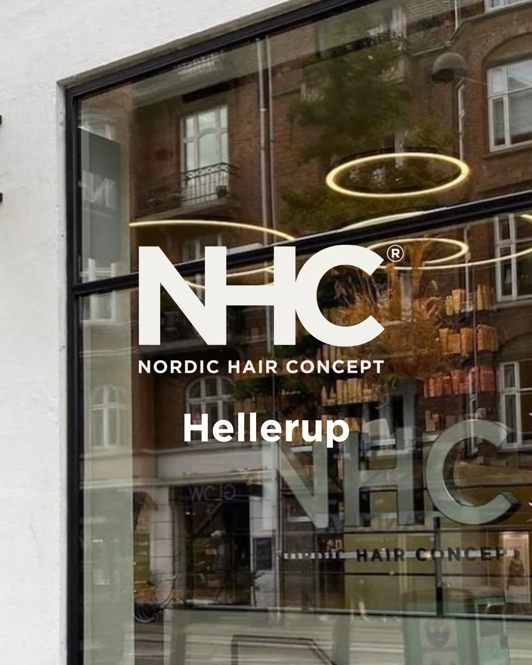 Nordic Hair Concept Hellerup. Reflekterende glasrude med tekst om en frisørsalon ved navn Nordic Hair Concept i Hellerup, med moderne belysning og bygninger i baggrunden.