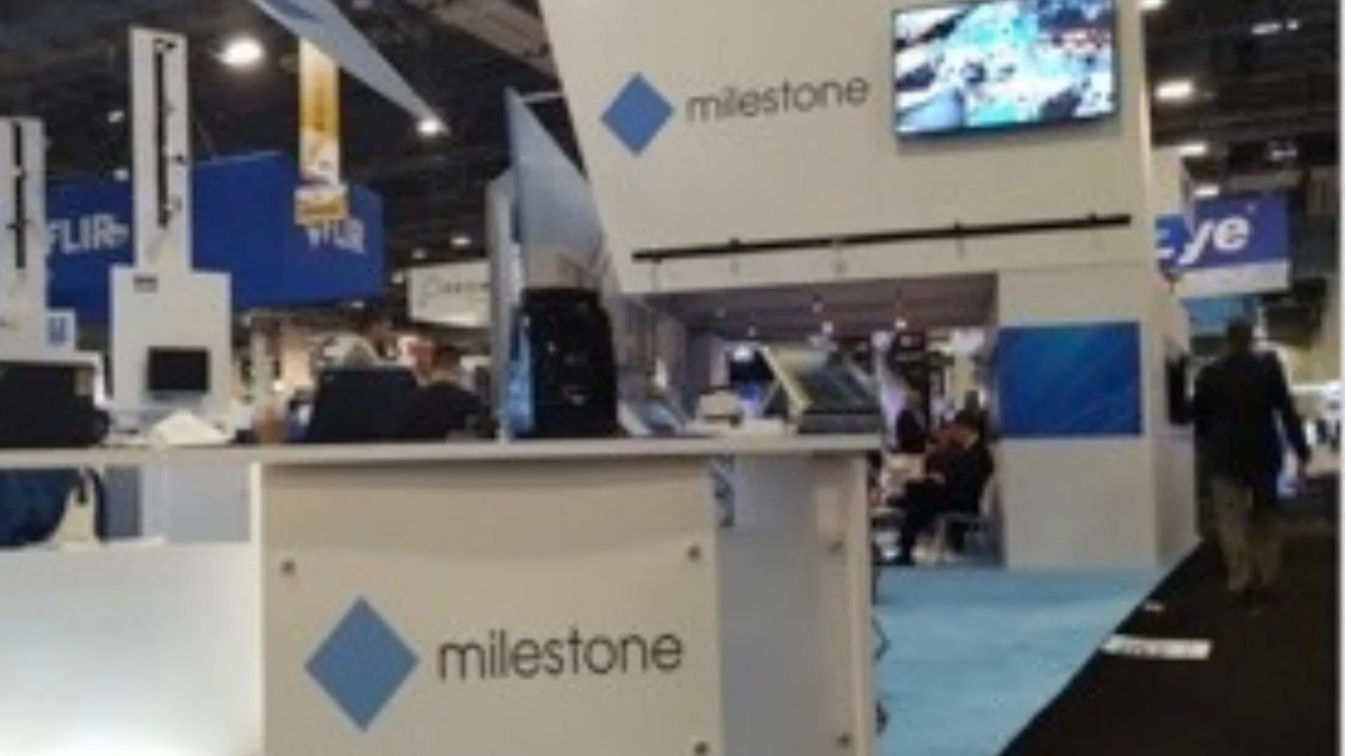 blurry image of a trade show booth for milestone plain white with blue carpet and blue logo
