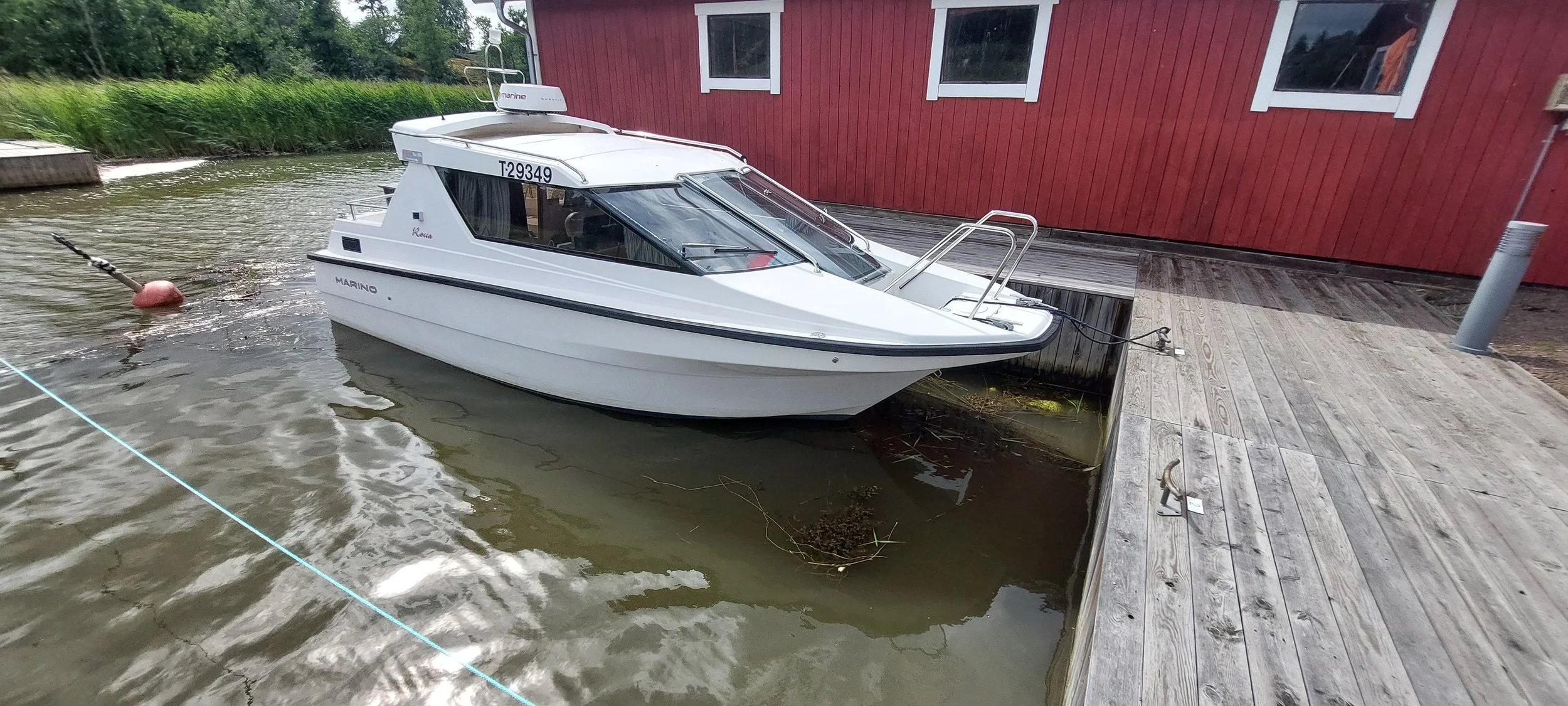 Small white motorboat docked at a wooden pier beside a red building.