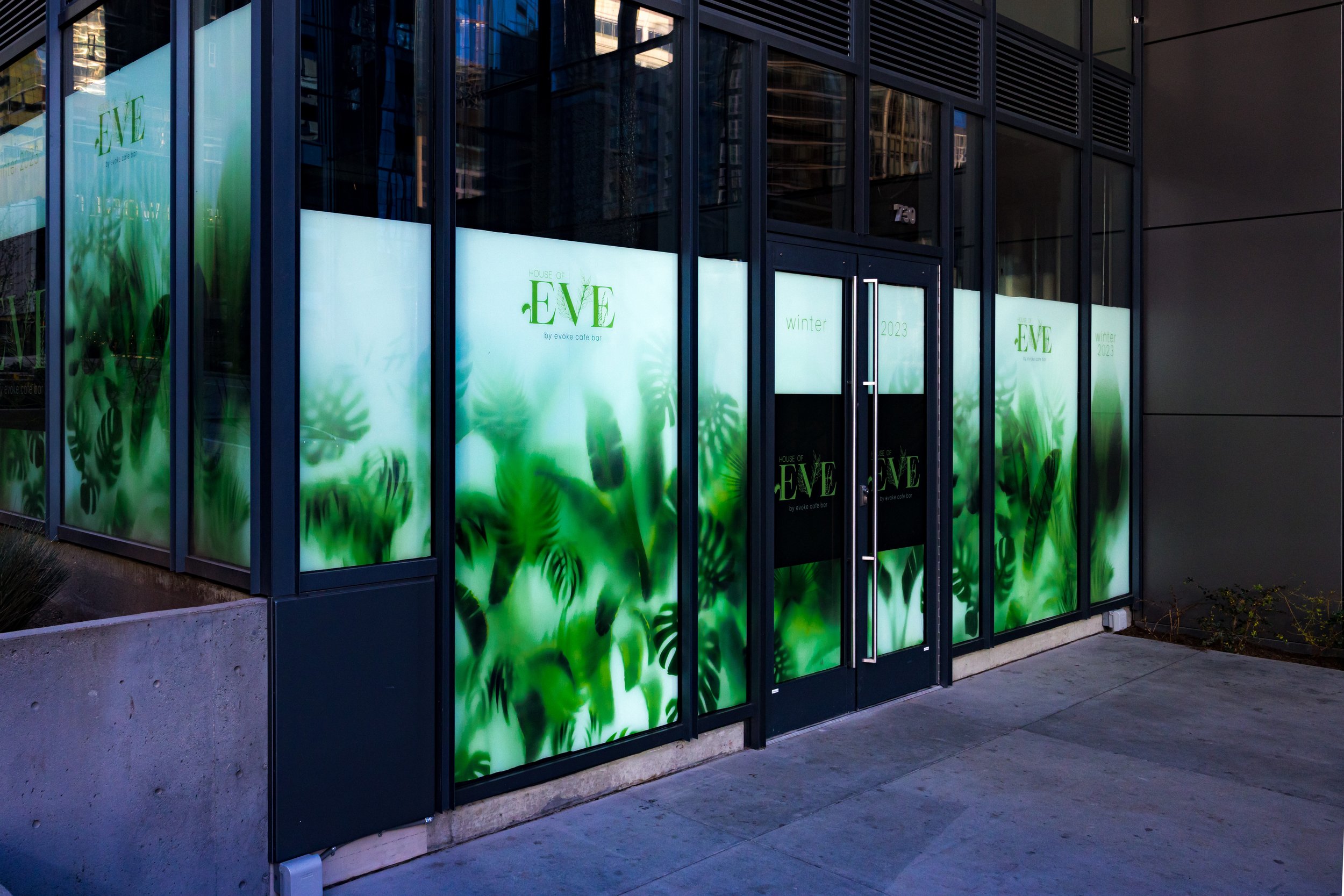 Large glass windows of a storefront with green leaf designs and the text 'House of Eve' and 'Winter 2023'.