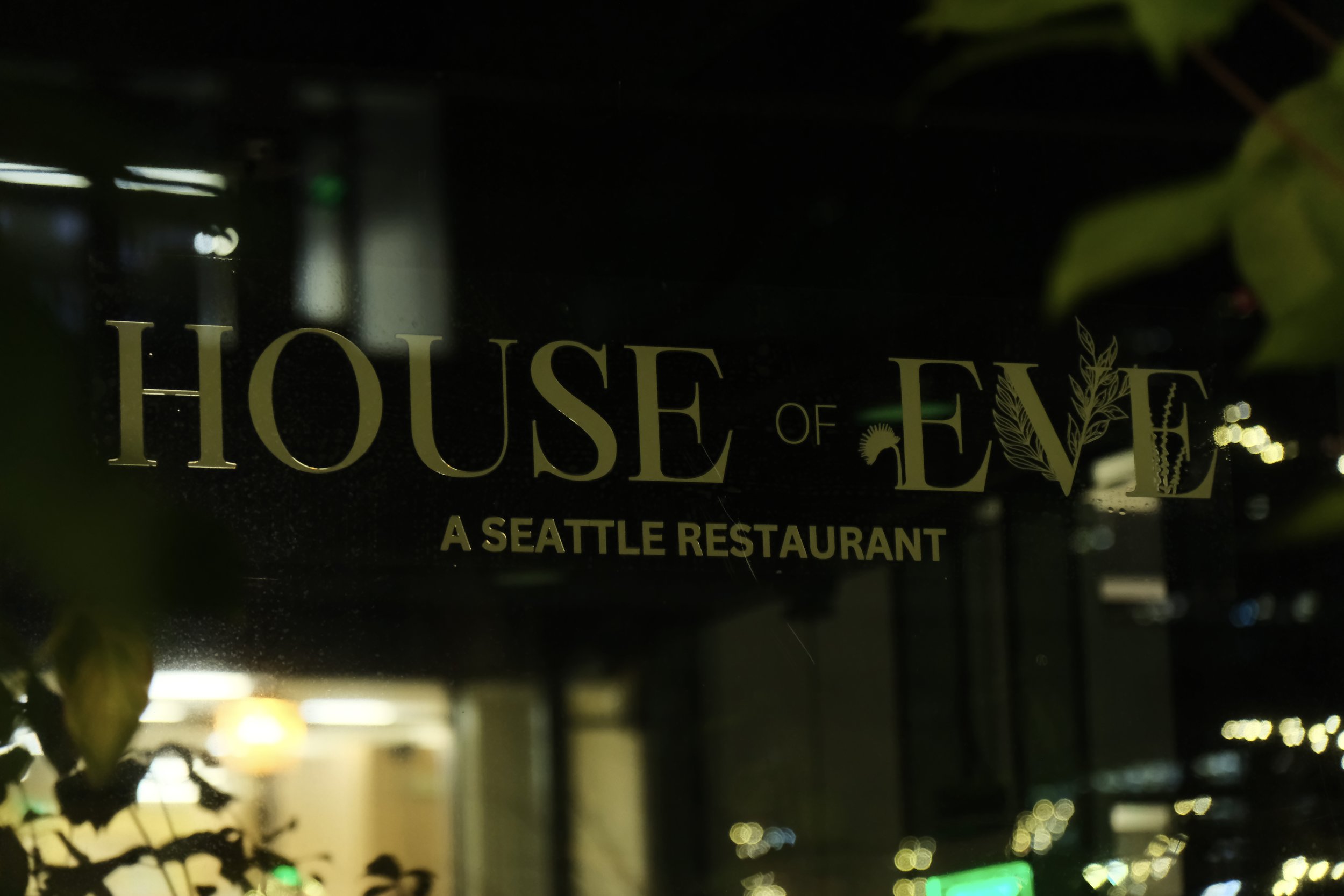 Sign for "House of Eve" with the subtitle "A Seattle Restaurant," surrounded by plant leaves.