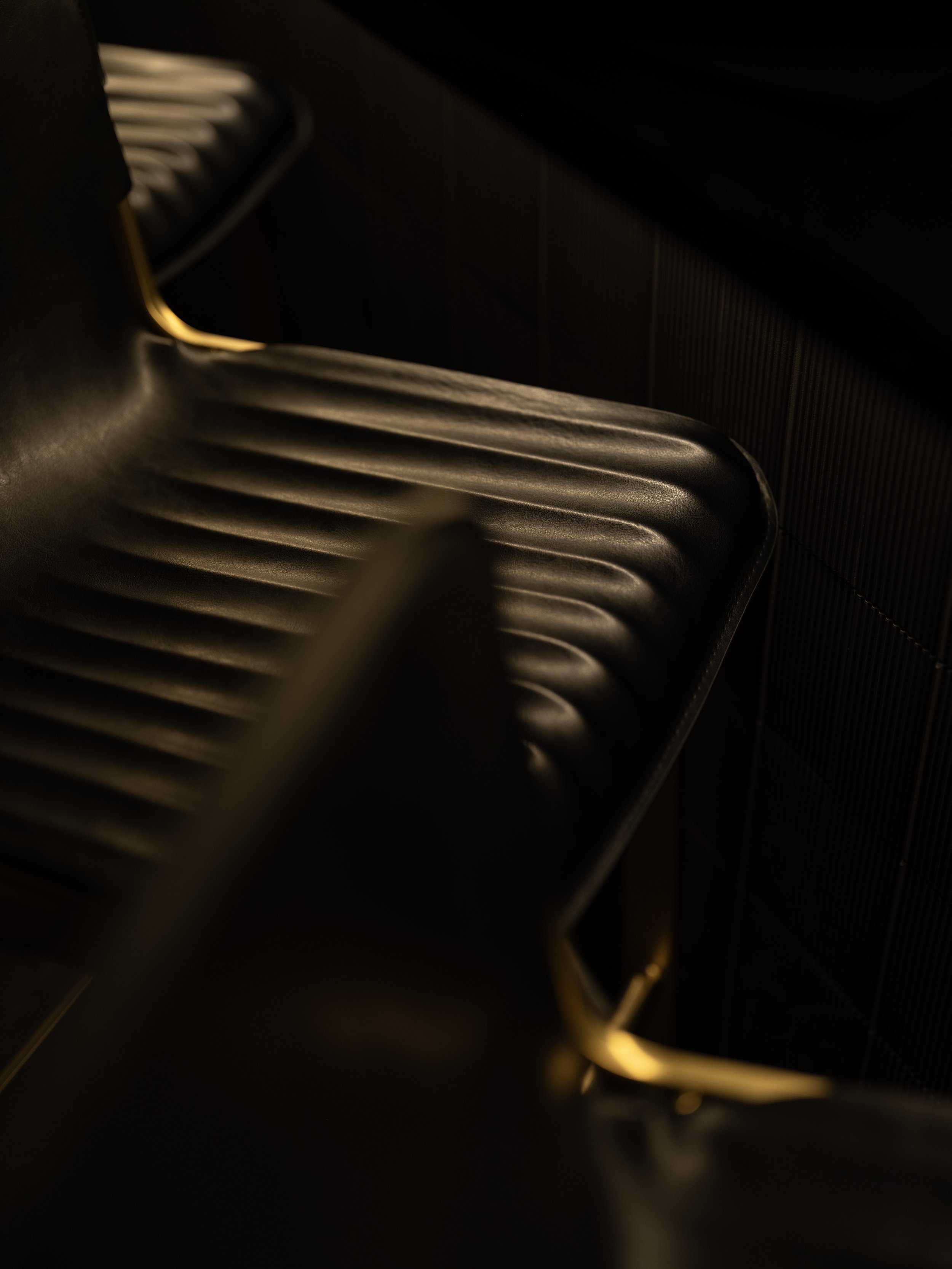 Close-up of a dark, ribbed leather chair with golden legs in dim lighting.