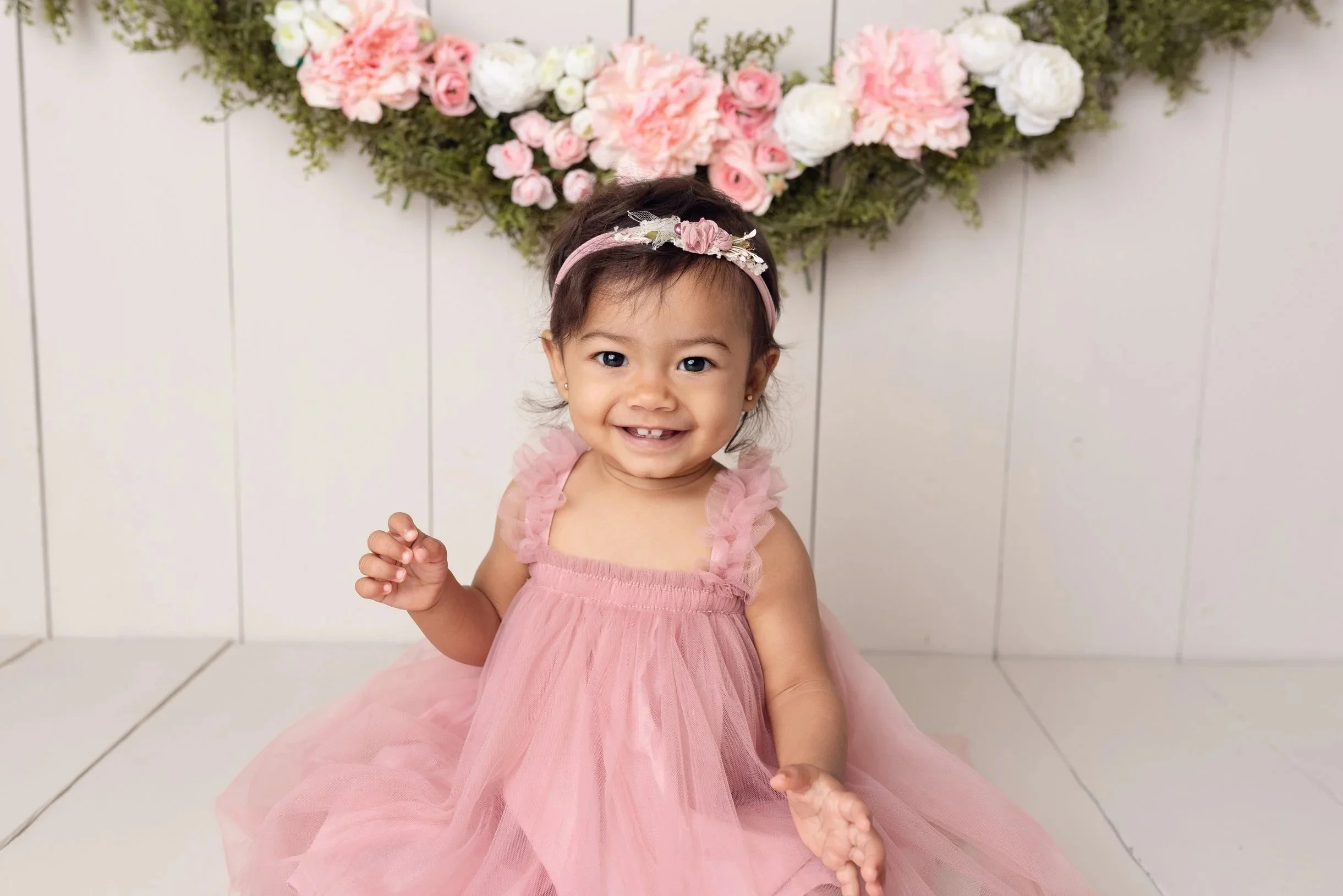 Toddler wearing a green romper and headband on beige background.
