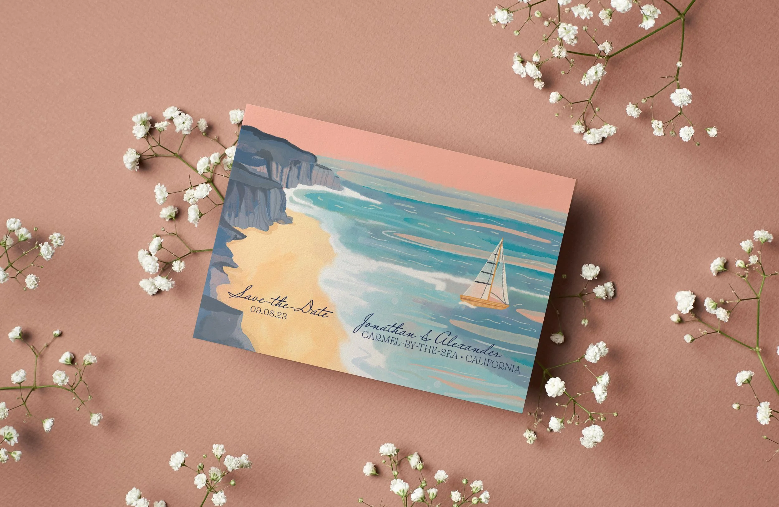 A watercolor-style beach wedding invitation with a cliff and sailboat illustration, surrounded by white baby's breath flowers on a pink background.