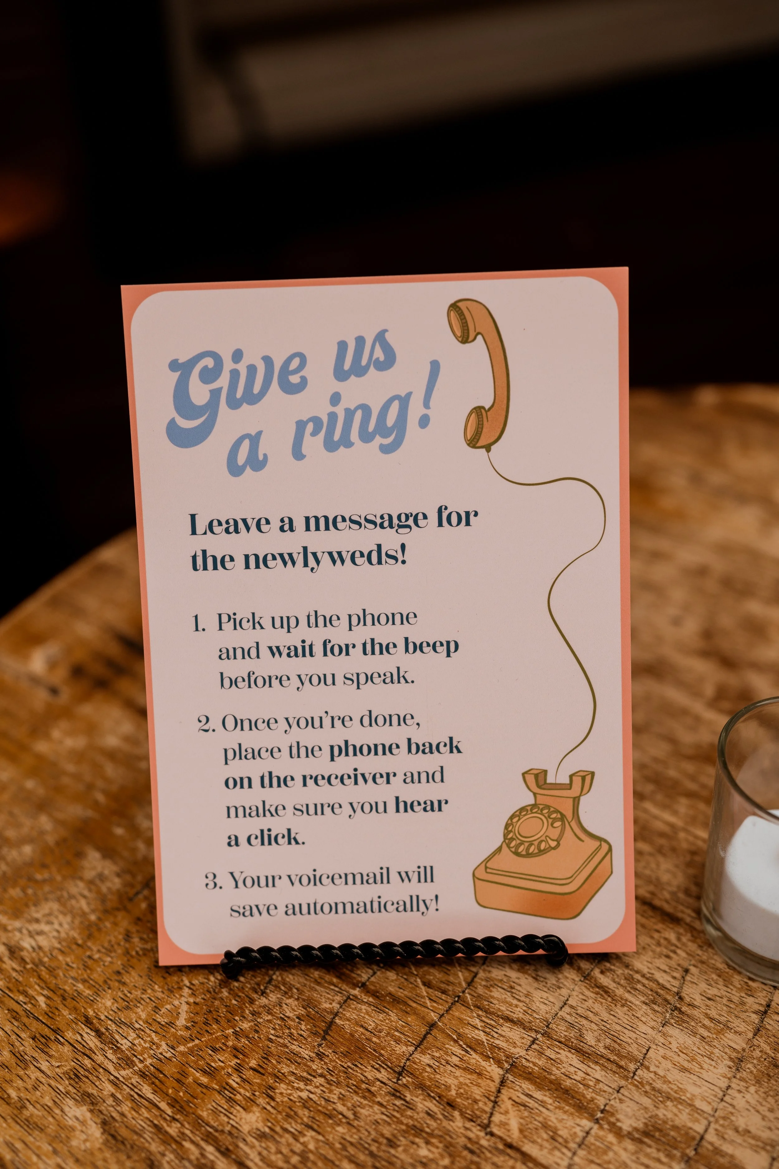 Sign with instructions for giving a phone number to newlyweds, titled "Give us a ring!" with an illustration of a vintage rotary phone.