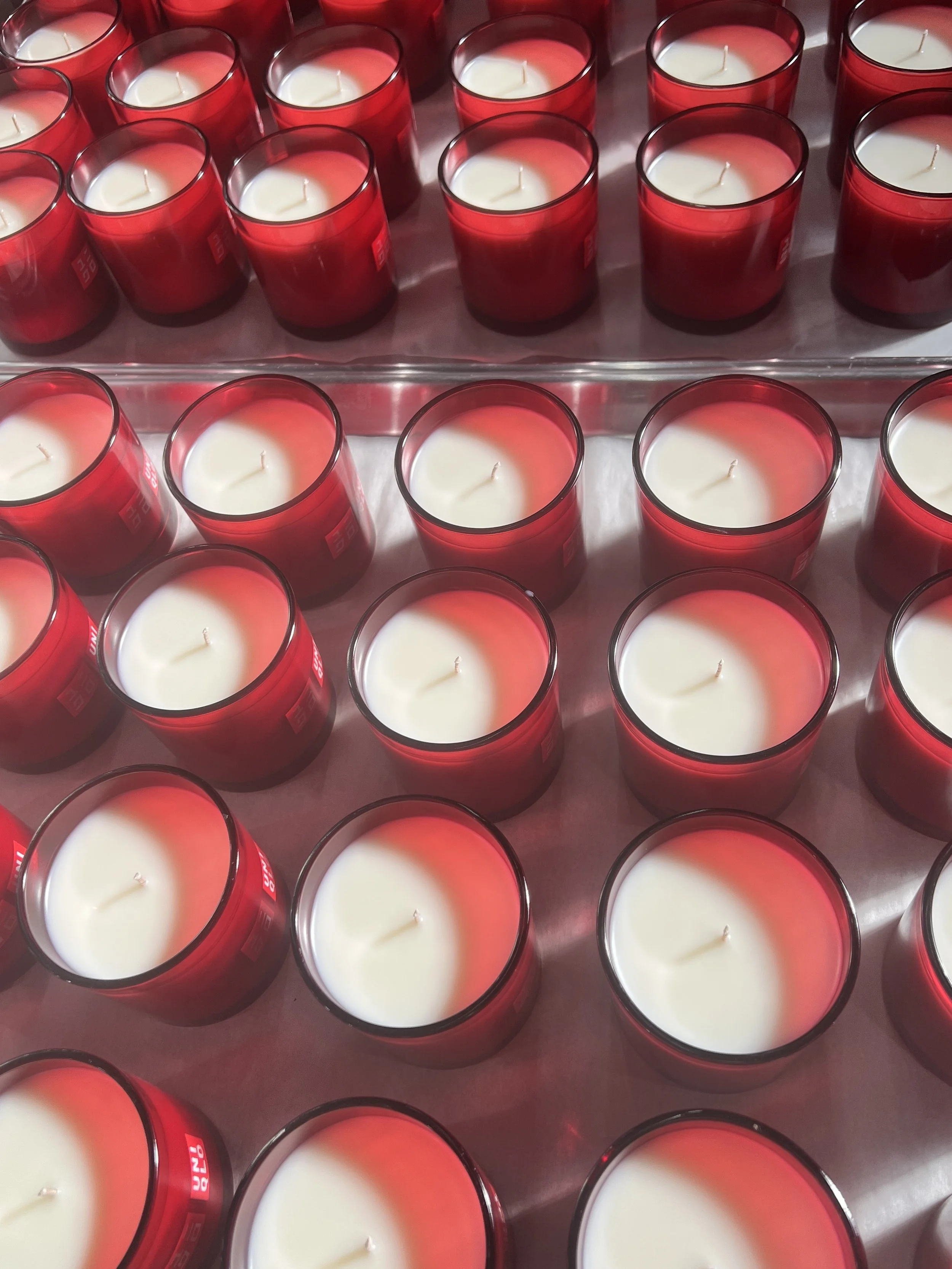 Rows of custom candles curing in red glass vessels during manufacturing for a private label brand